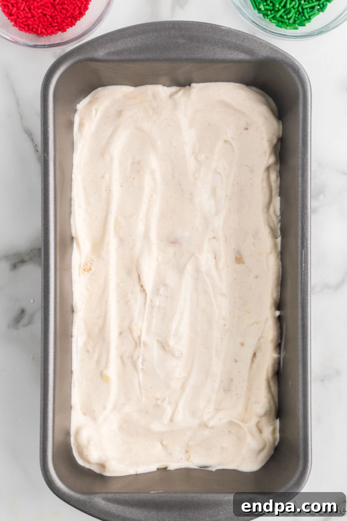 Merry Melts 10 A layer of Christmas ice cream mixture being spread into a loaf pan, topped with sprinkles.