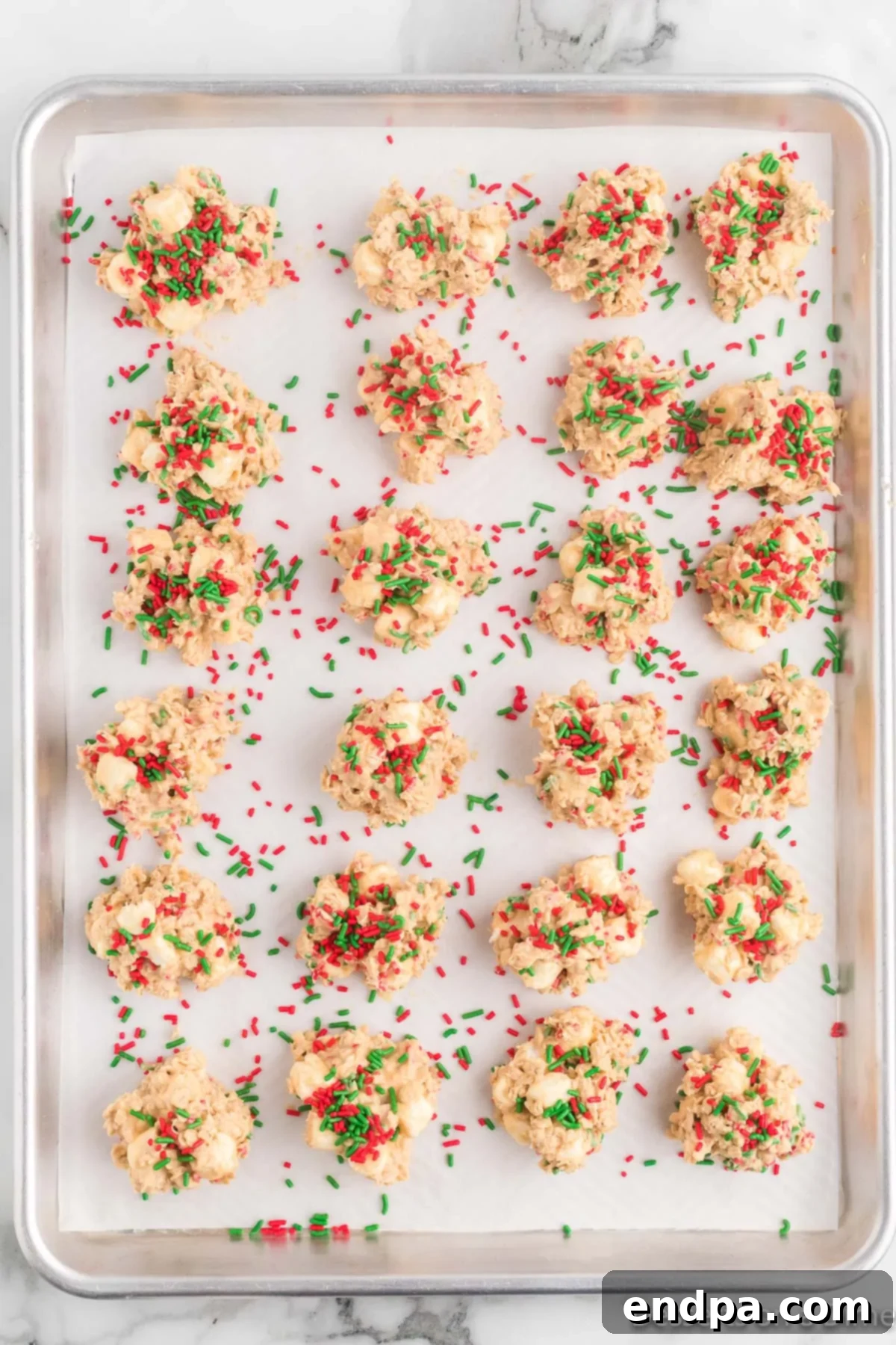 Festive No-Bake Delights 7 Freshly dropped Christmas No Bake Cookies on a baking sheet, topped with remaining festive sprinkles.