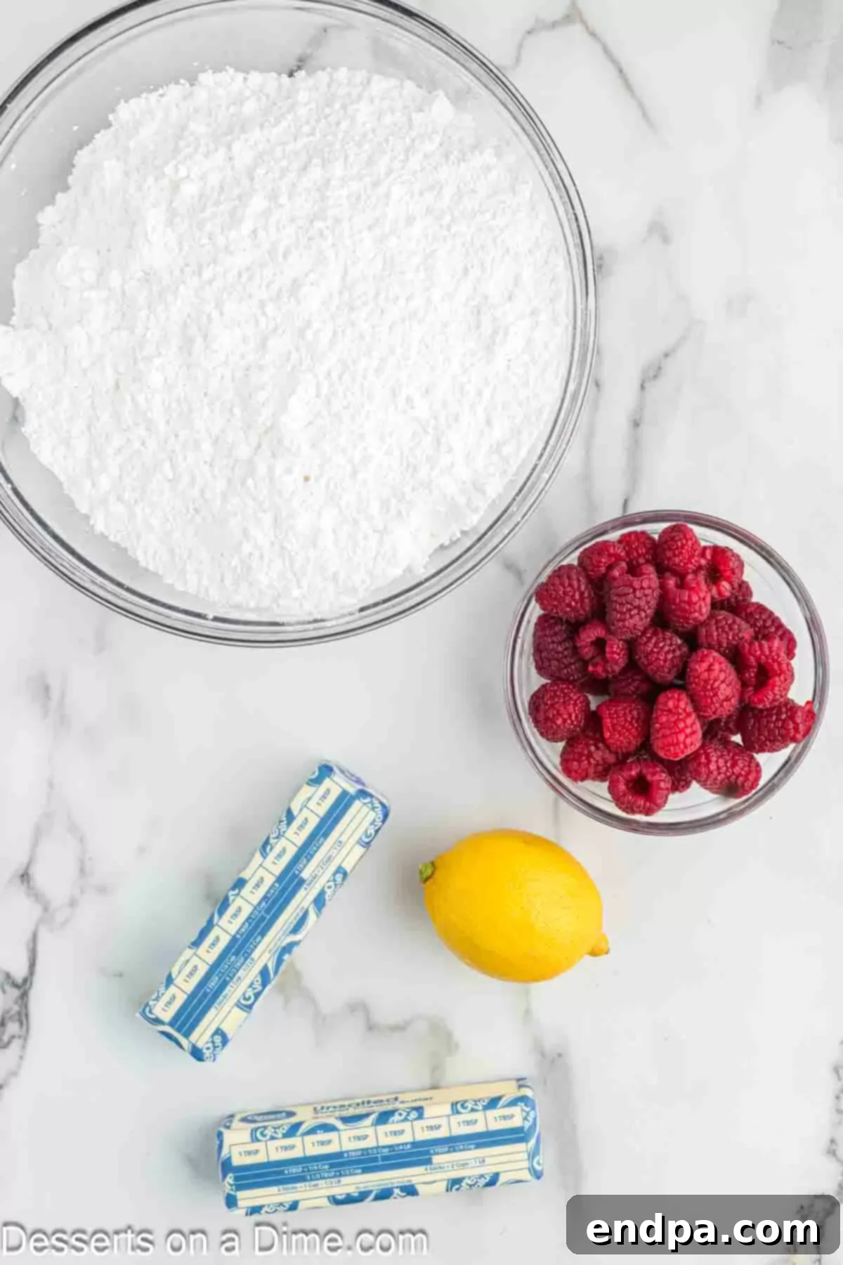 Ingredients for Raspberry frosting - fresh raspberries, lemon, softened unsalted butter, and powdered sugar, laid out on a clean surface.