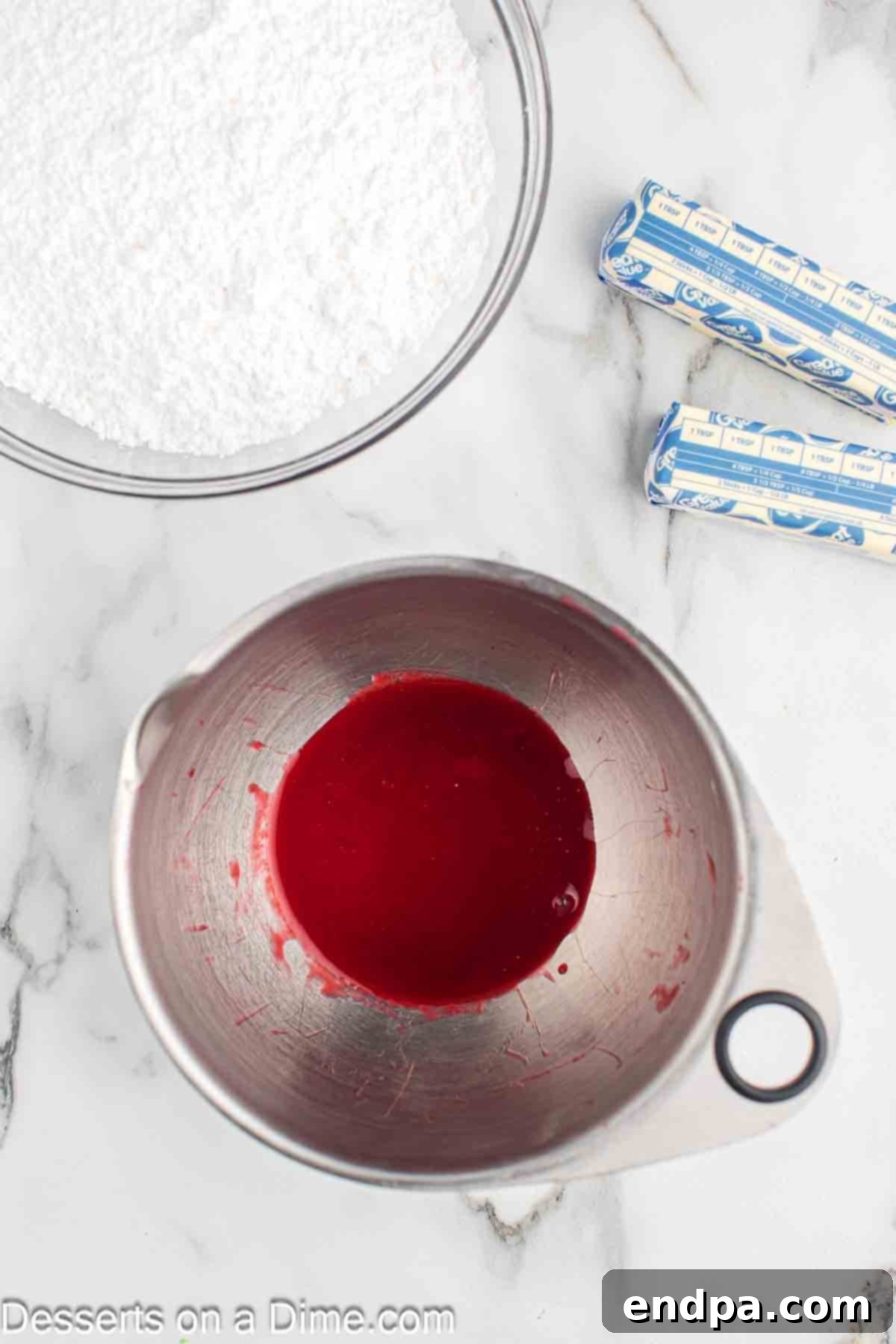 Raspberry puree being pressed through a fine mesh strainer into a bowl to remove seeds.