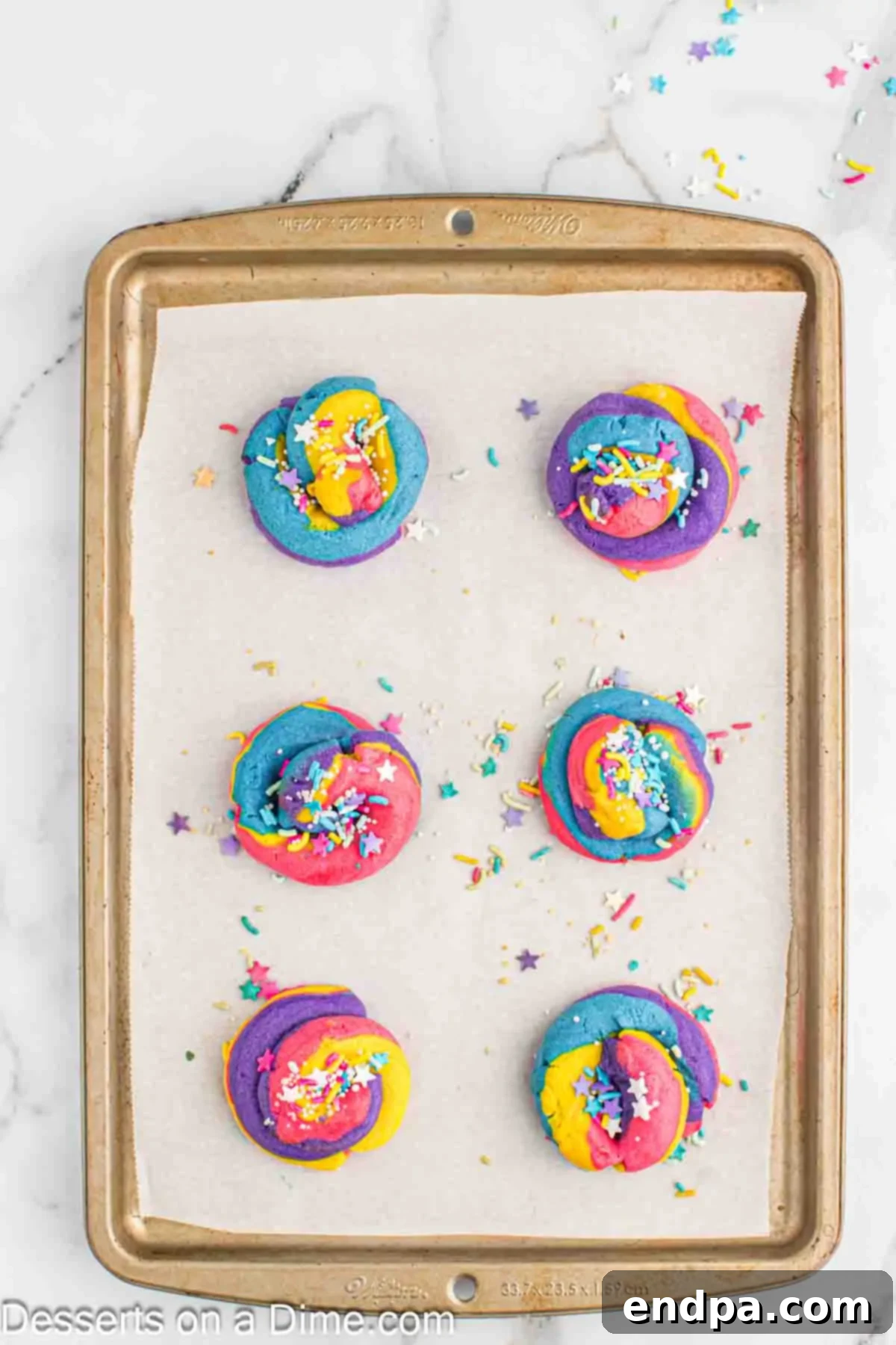 Rainbow Unicorn Drops 11 Unicorn Poop Cookies on a baking sheet, generously topped with an assortment of star and multi-colored sprinkles.