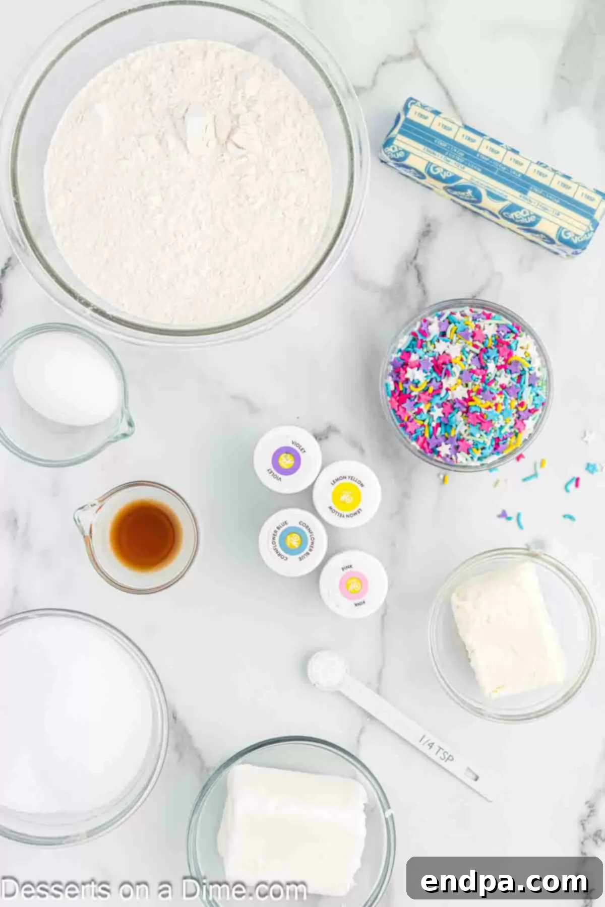 Rainbow Unicorn Drops 3 A selection of key ingredients for Unicorn Poop Cookies including cream cheese, food coloring, vanilla extract, flour, sprinkles, and butter.