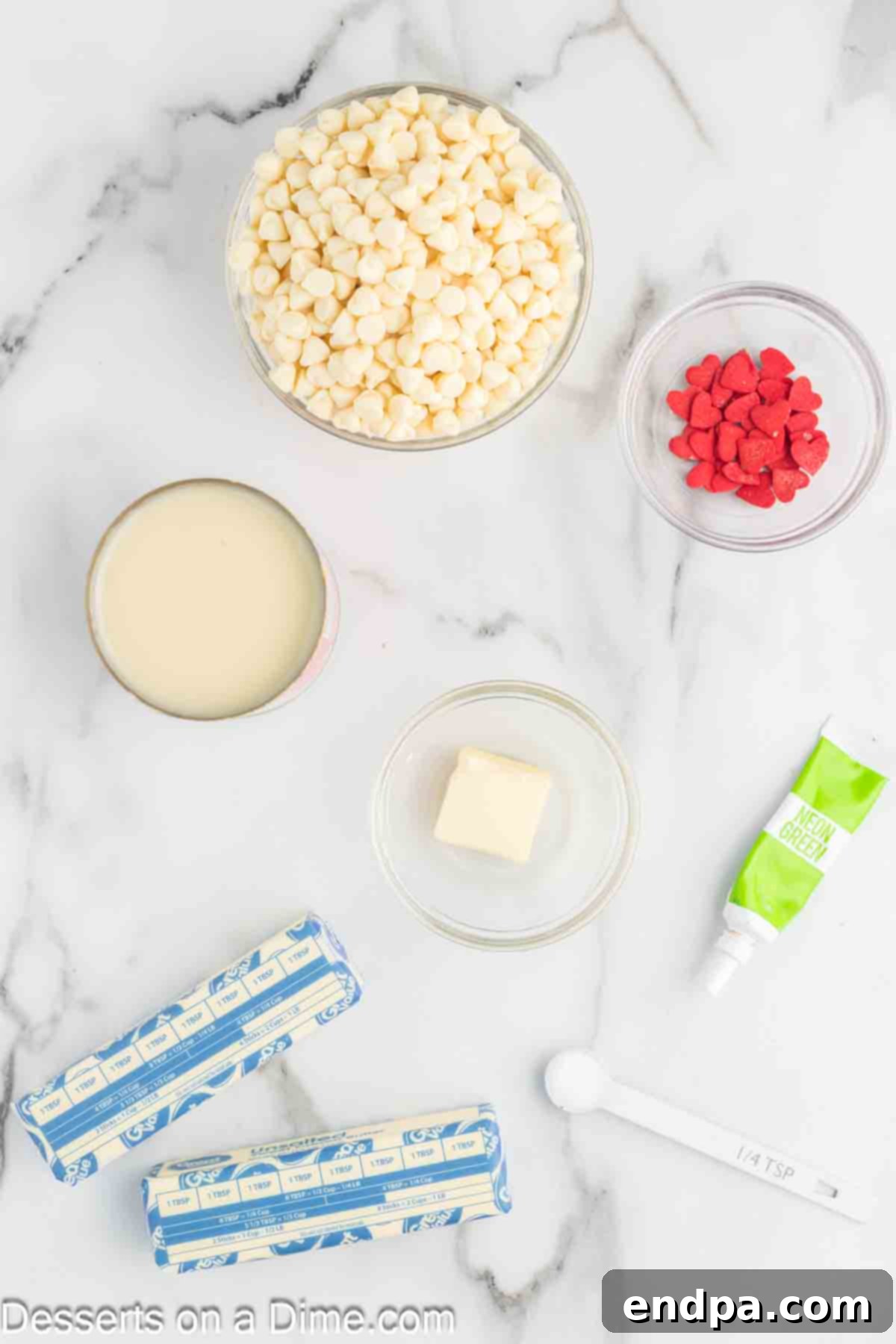 Ingredients for Grinch Fudge: White Chocolate Chips, sweetened condensed milk, salt, butter, green food coloring, red heart sprinkles arranged for a photo.