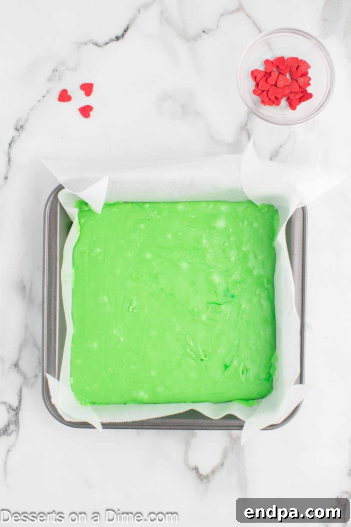 Pouring the melted green chocolate fudge mixture into a prepared baking pan.