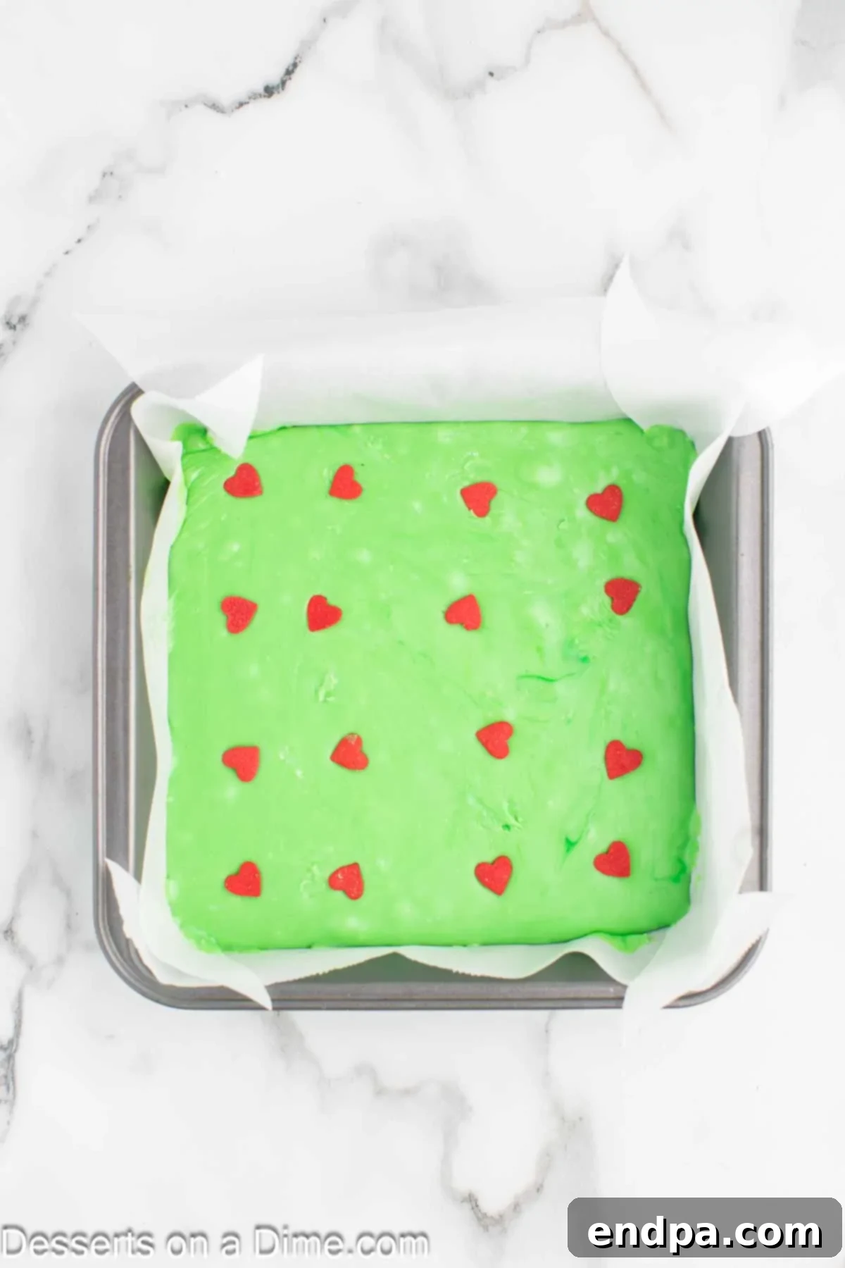 Topping the melted green chocolate fudge with festive red heart sprinkles.