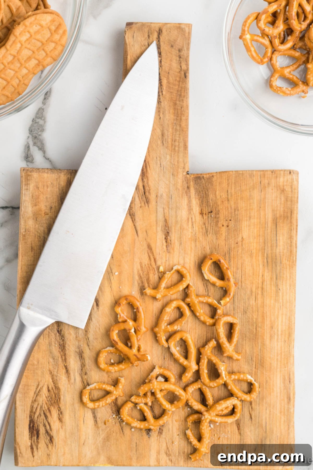 A hand carefully cutting mini pretzels in half on a cutting board with a knife for reindeer antlers.