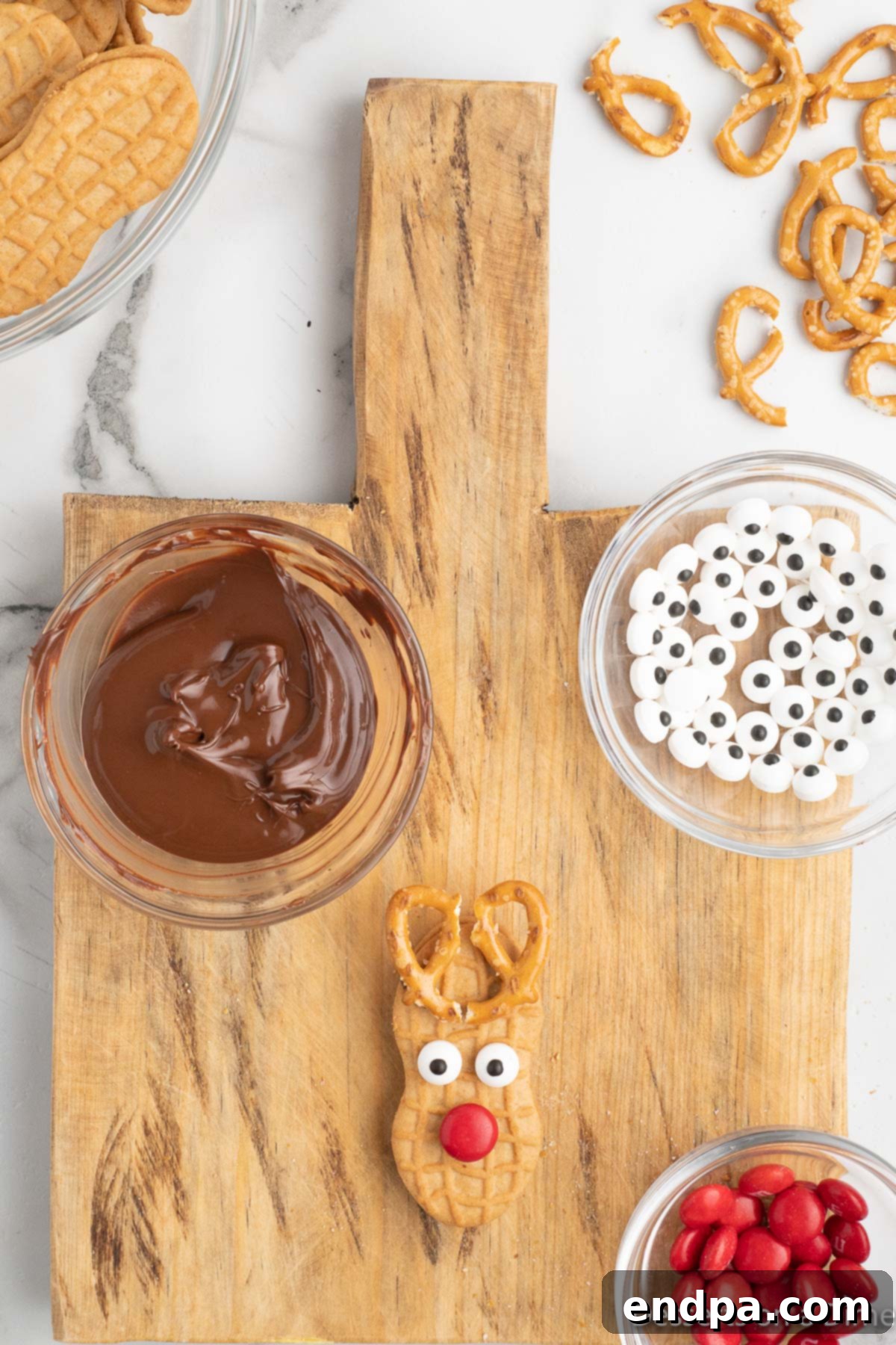 Decorating a Nutter Butter cookie by placing candy eyes and a red M&M nose using melted chocolate.
