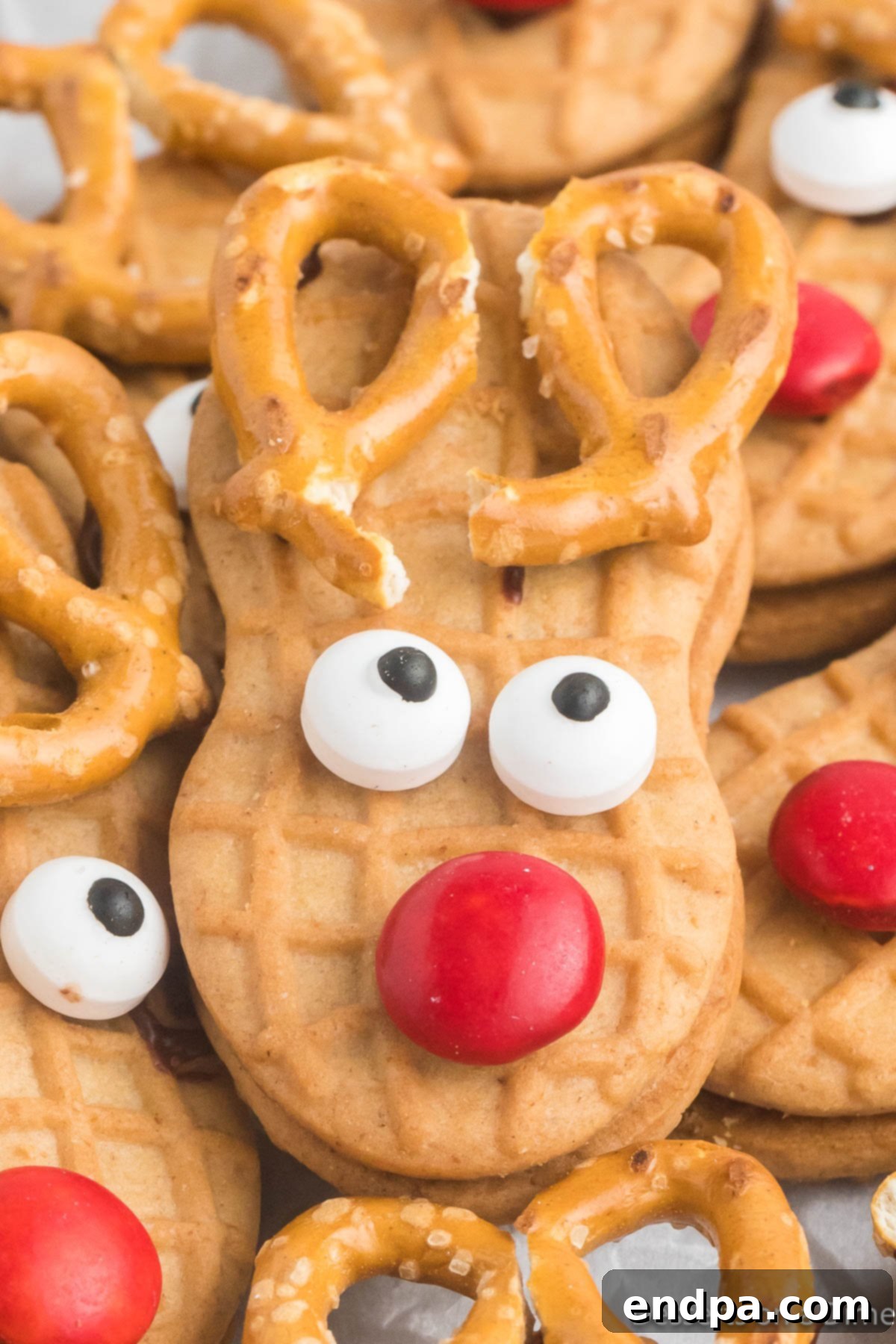 Close-up photo of a decorated Nutter Butter Reindeer cookie, showing detail of the candy eyes, red M&M nose, and pretzel antlers.