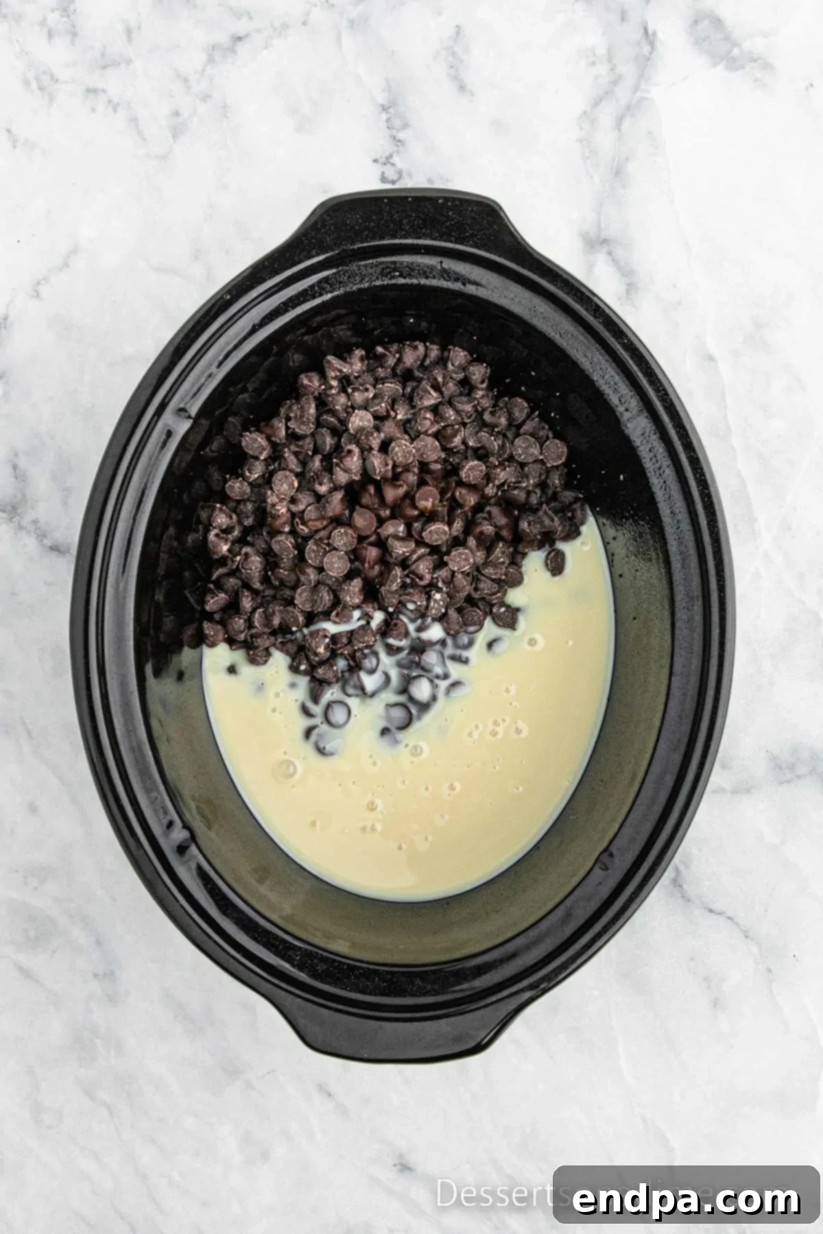 Crockpot with sweetened condensed milk, chocolate chips, and vanilla extract combined, ready to cook.