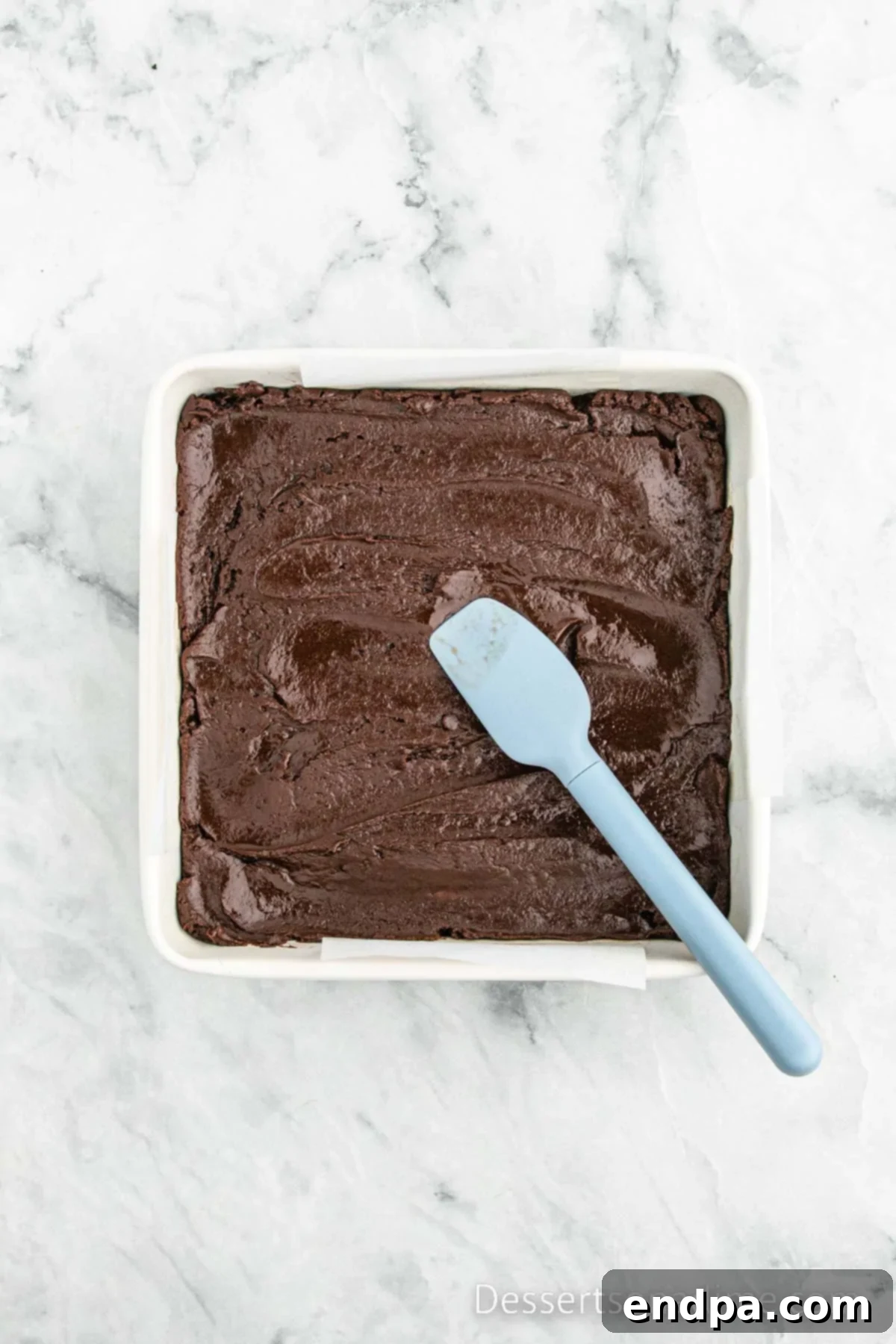Smooth chocolate fudge mixture spread evenly in a parchment-lined baking dish.