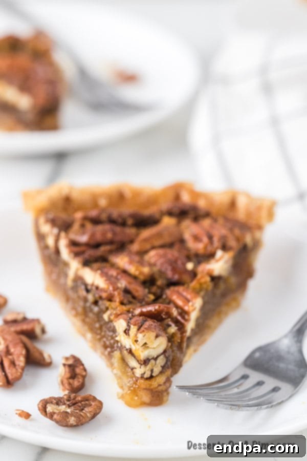 How to Freeze Pecan Pie 3 A close-up shot of a single slice of pecan pie, showcasing its golden-brown crust and sticky, nutty filling, resting on a white plate with a fork beside it.