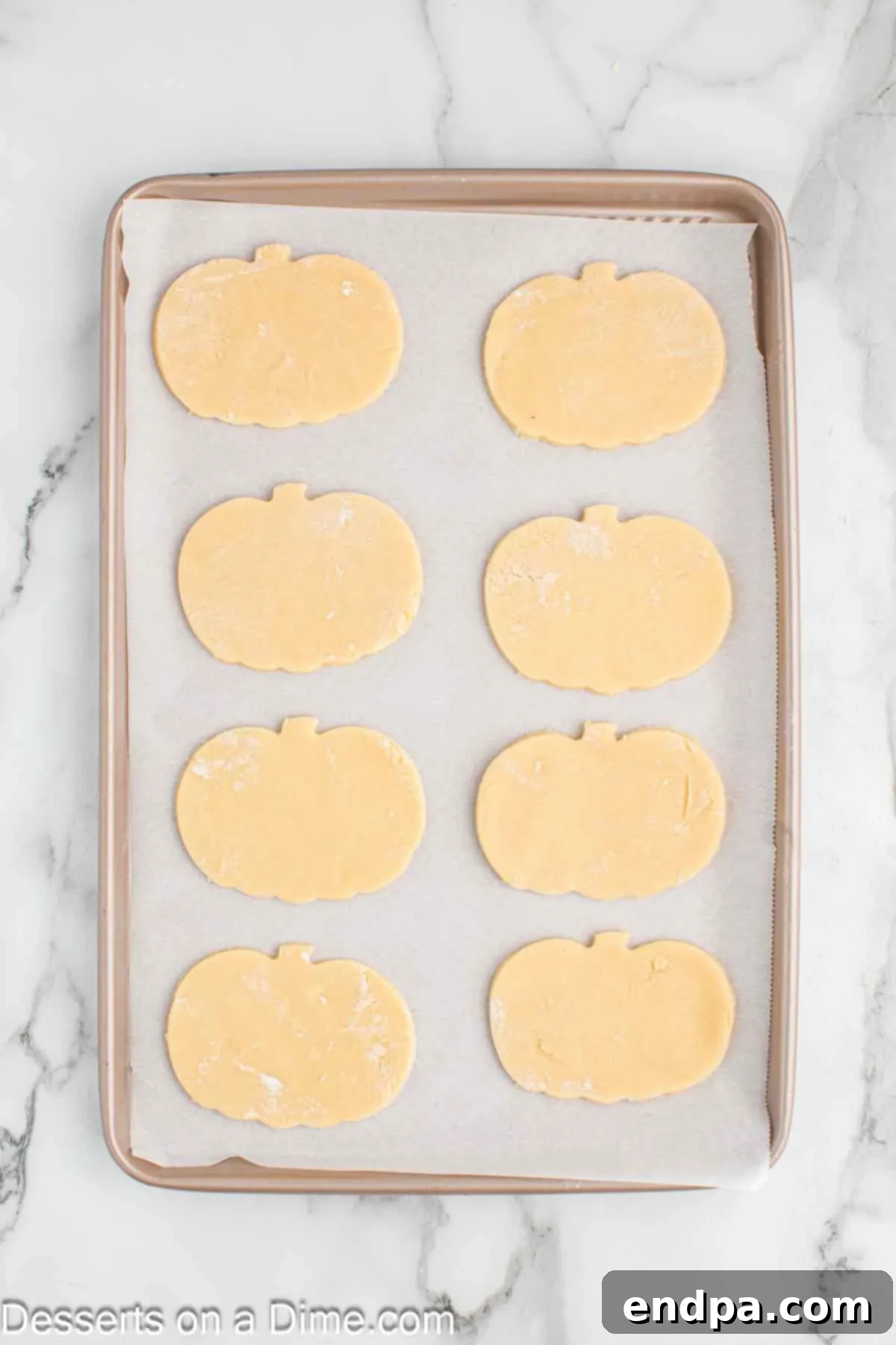 Frightfully Delicious Halloween Cookies 8 Pumpkin-shaped sugar cookies arranged on a baking sheet lined with parchment paper.