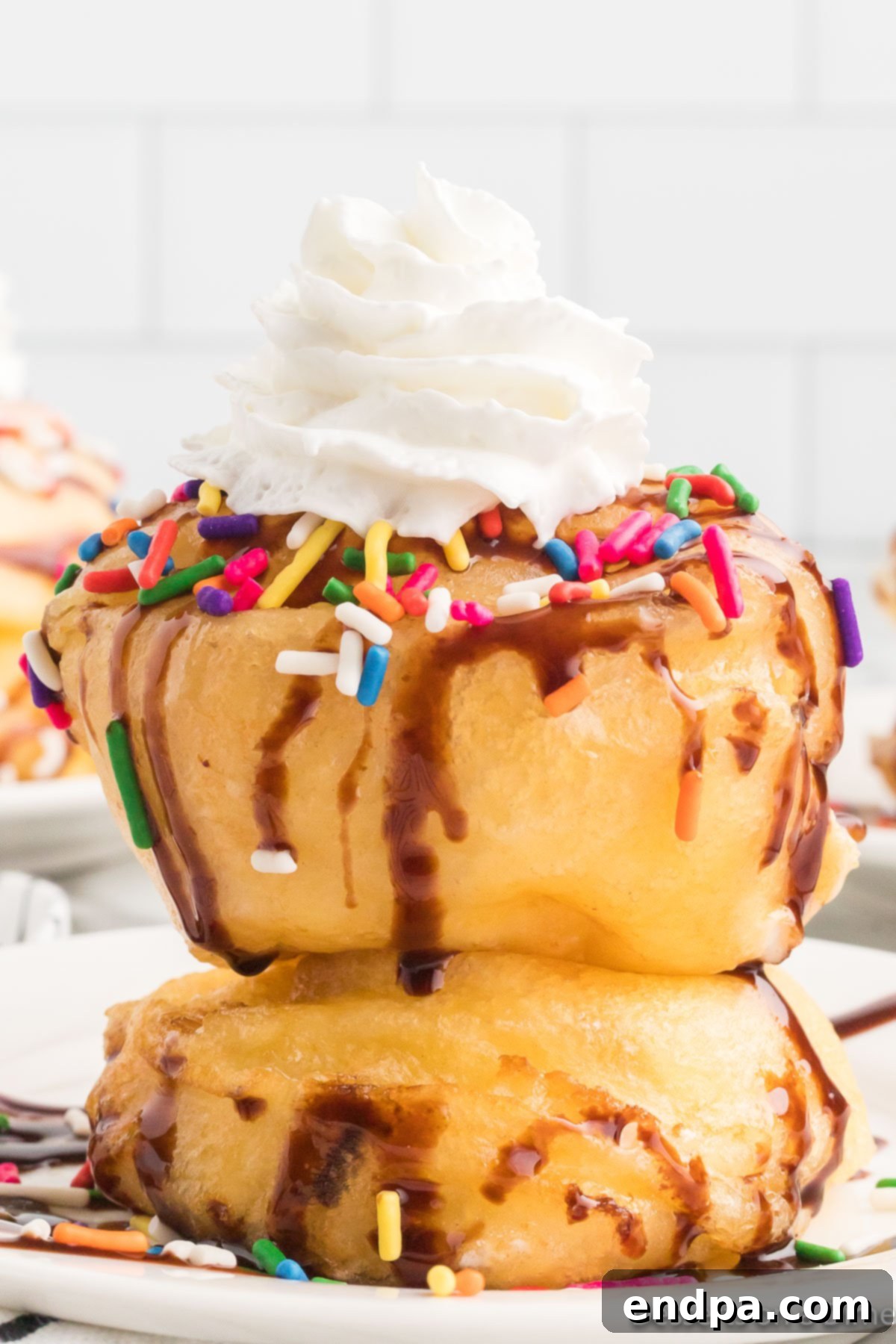 Deep Fried Marshmallows topped with chocolate sauce, whipped topping and sprinkles on a plate. 