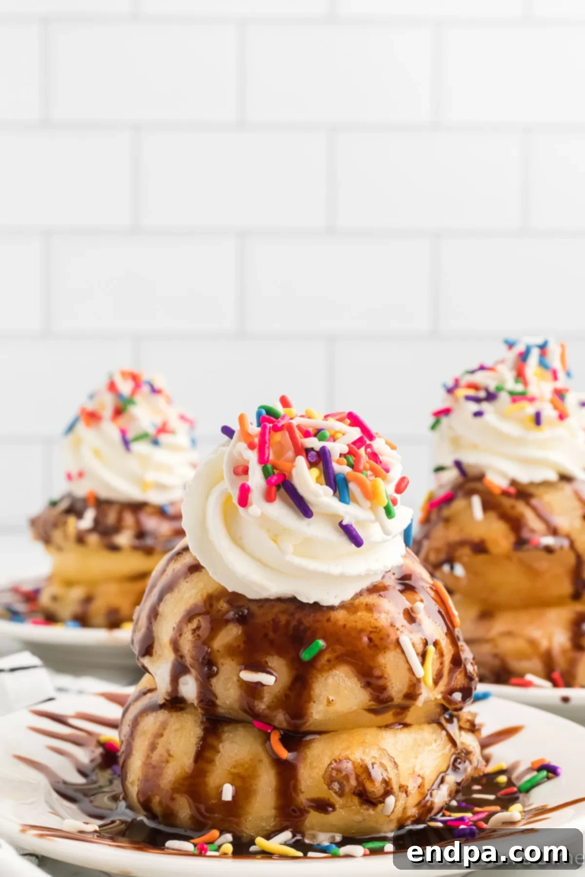 Deep Fried Marshmallows topped with chocolate sauce, whipped topping and sprinkles on a plate. 