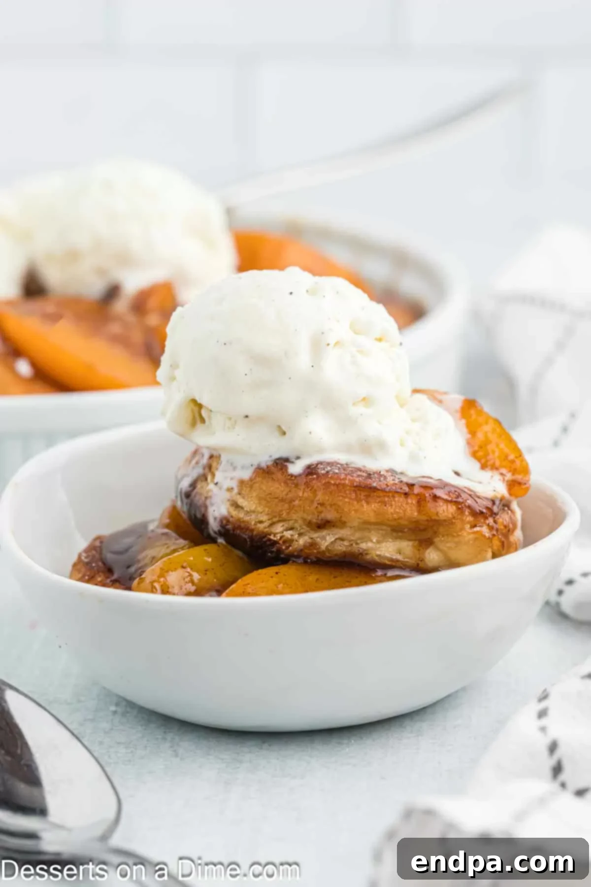Close-up of a serving of deep fried peach cobbler with melted vanilla ice cream, showing the flaky texture of the fried biscuit and the rich peach sauce.