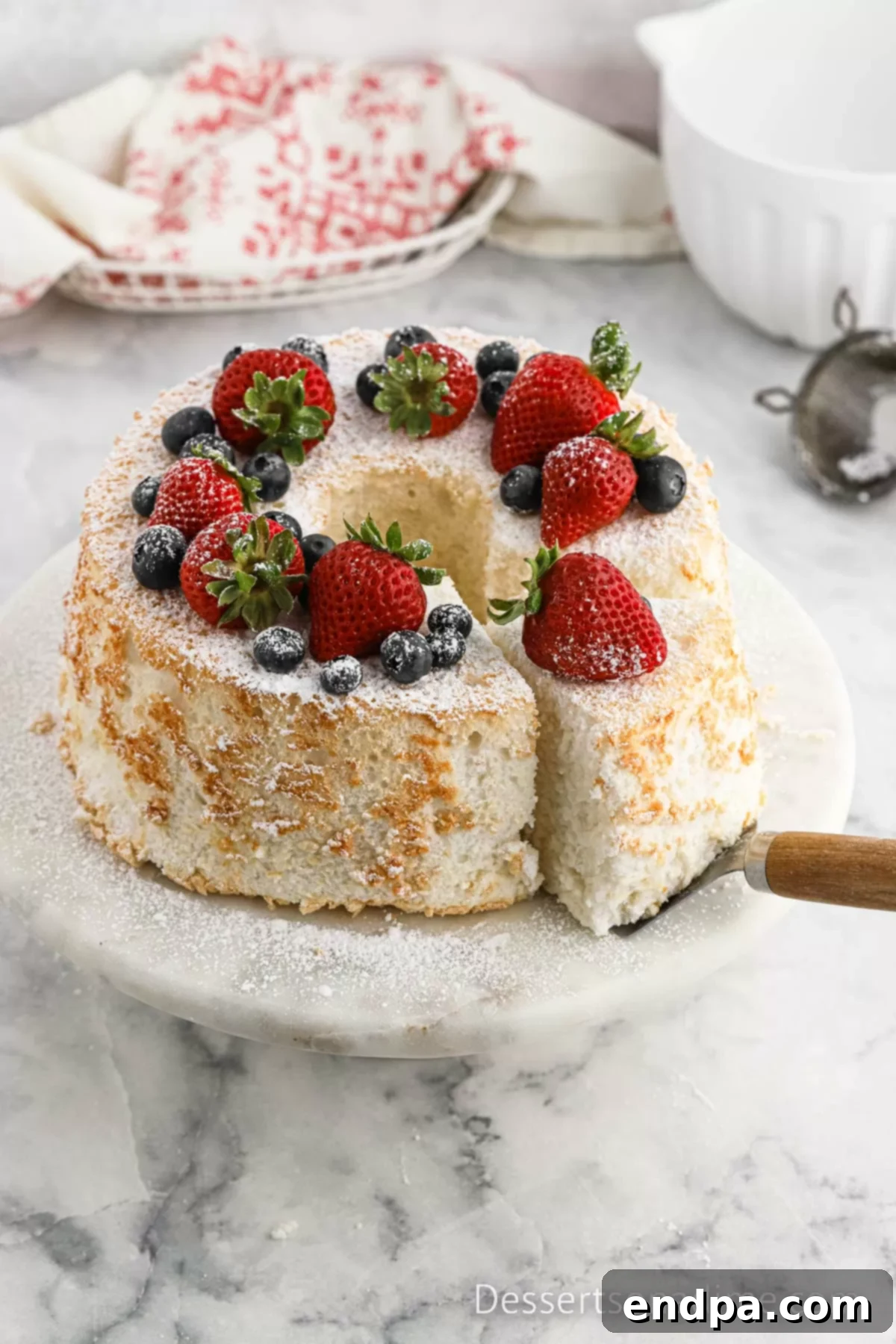 Angel Food Cake on a cake stand with fresh fruit on top, showcasing its light and airy texture.