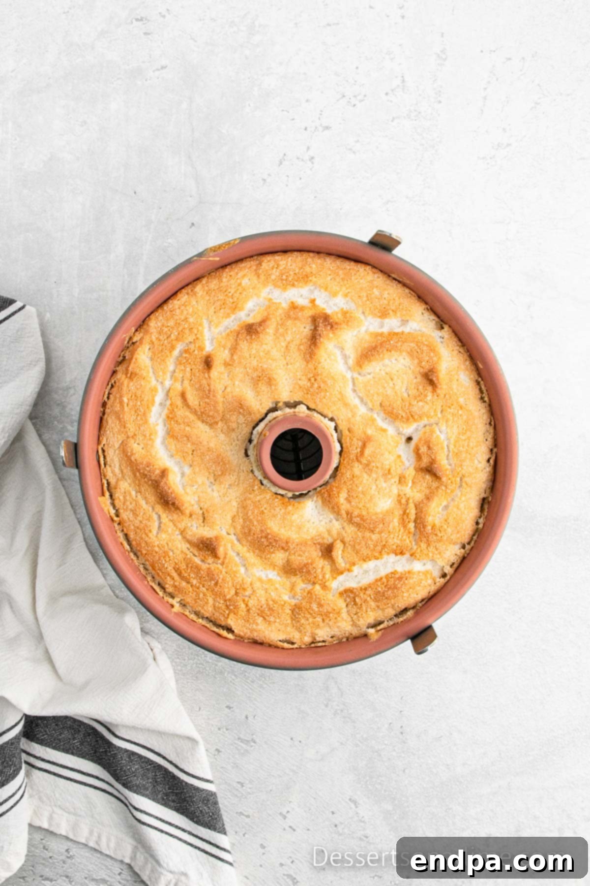 Baked Angel Food Cake cooling upside down on a wire rack in its tube pan.