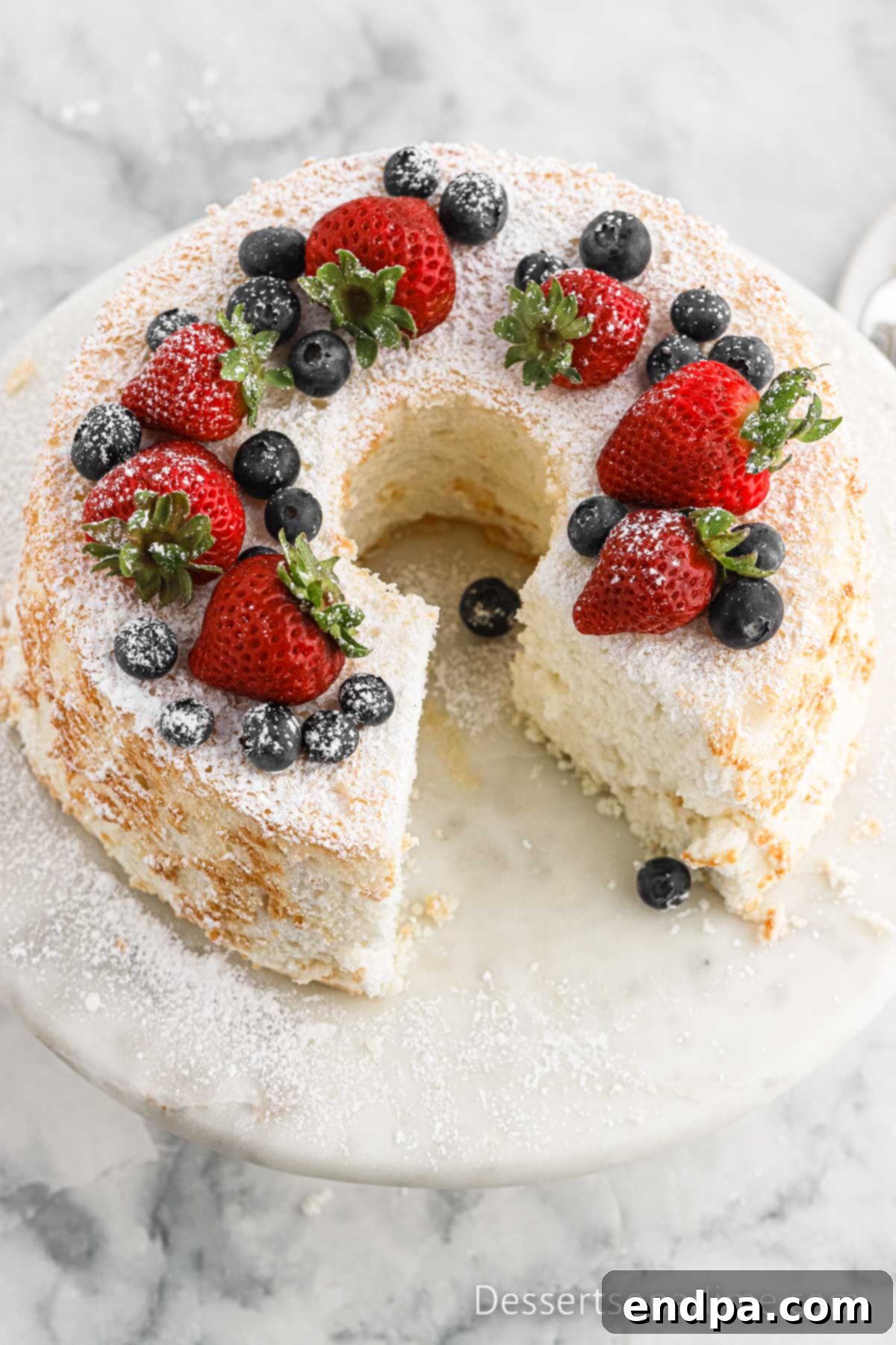 Angel Food Cake on a cake stand with an abundance of fresh fruit, including strawberries, blueberries, and raspberries, illustrating perfect topping pairings.