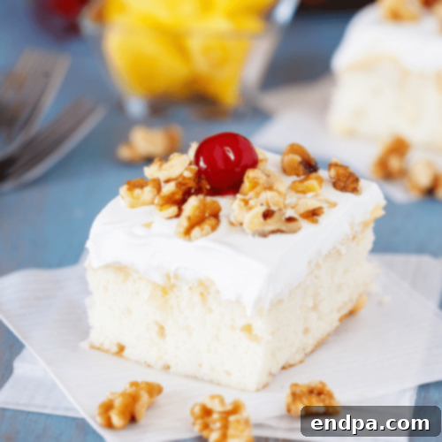A slice of Pineapple Pudding Cake, showcasing the white cake layers, pineapple pudding filling, and a cherry on top.