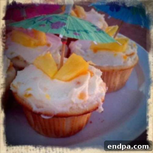 Aloha Cupcakes garnished with pineapple wedges and tropical umbrellas, bursting with fruit flavors.