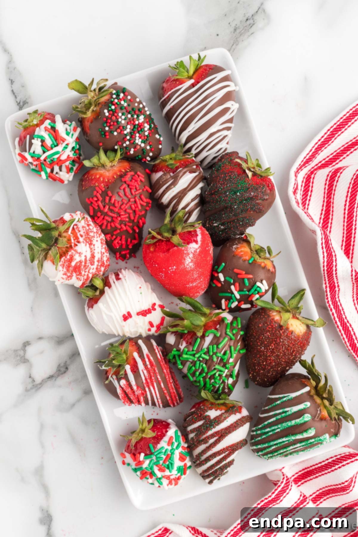 Yuletide Chocolate Strawberries 2 Vibrant Christmas Chocolate Covered Strawberries arranged artfully on a white platter, adorned with festive sprinkles.