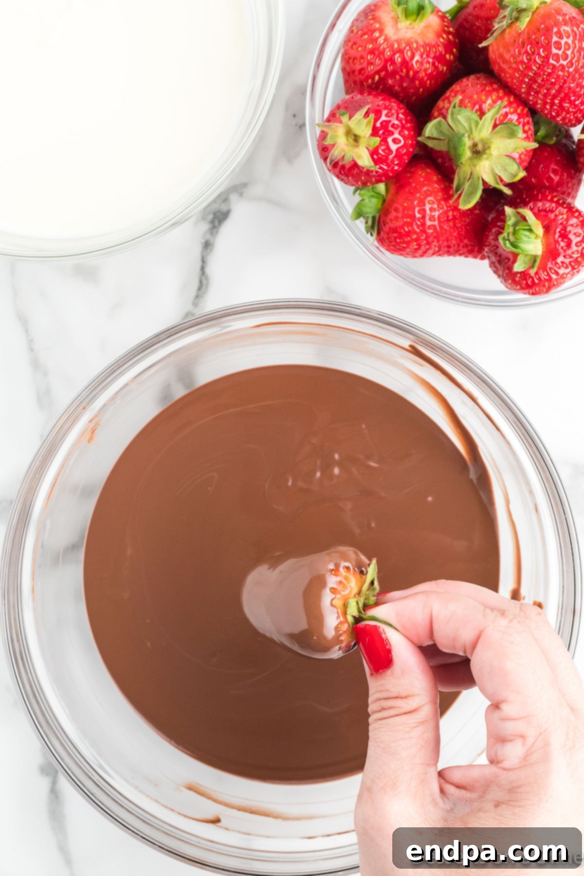 Yuletide Chocolate Strawberries 5 Fresh strawberry being dipped into a bowl of melted chocolate.