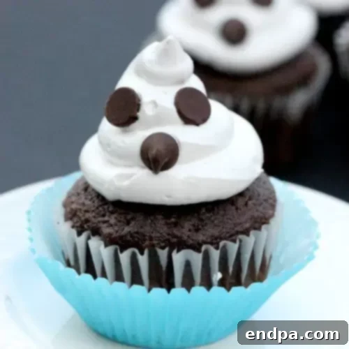 A trio of cute ghost cupcakes decorated with white frosting and chocolate chip eyes.