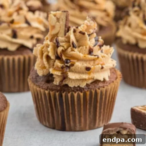 Rich Snickers Cupcakes topped with peanut butter frosting, a caramel drizzle, and chopped Snickers pieces.