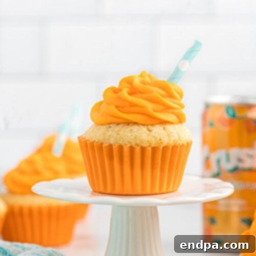 A vibrant Orange Crush Cupcake on a white plate, topped with orange soda-flavored icing.