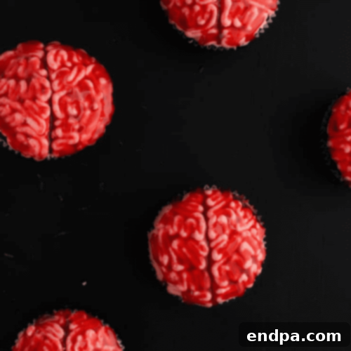 Gruesomely delightful Brain Cupcakes topped with pink frosting piped to resemble a brain, with a hint of red 'blood'.