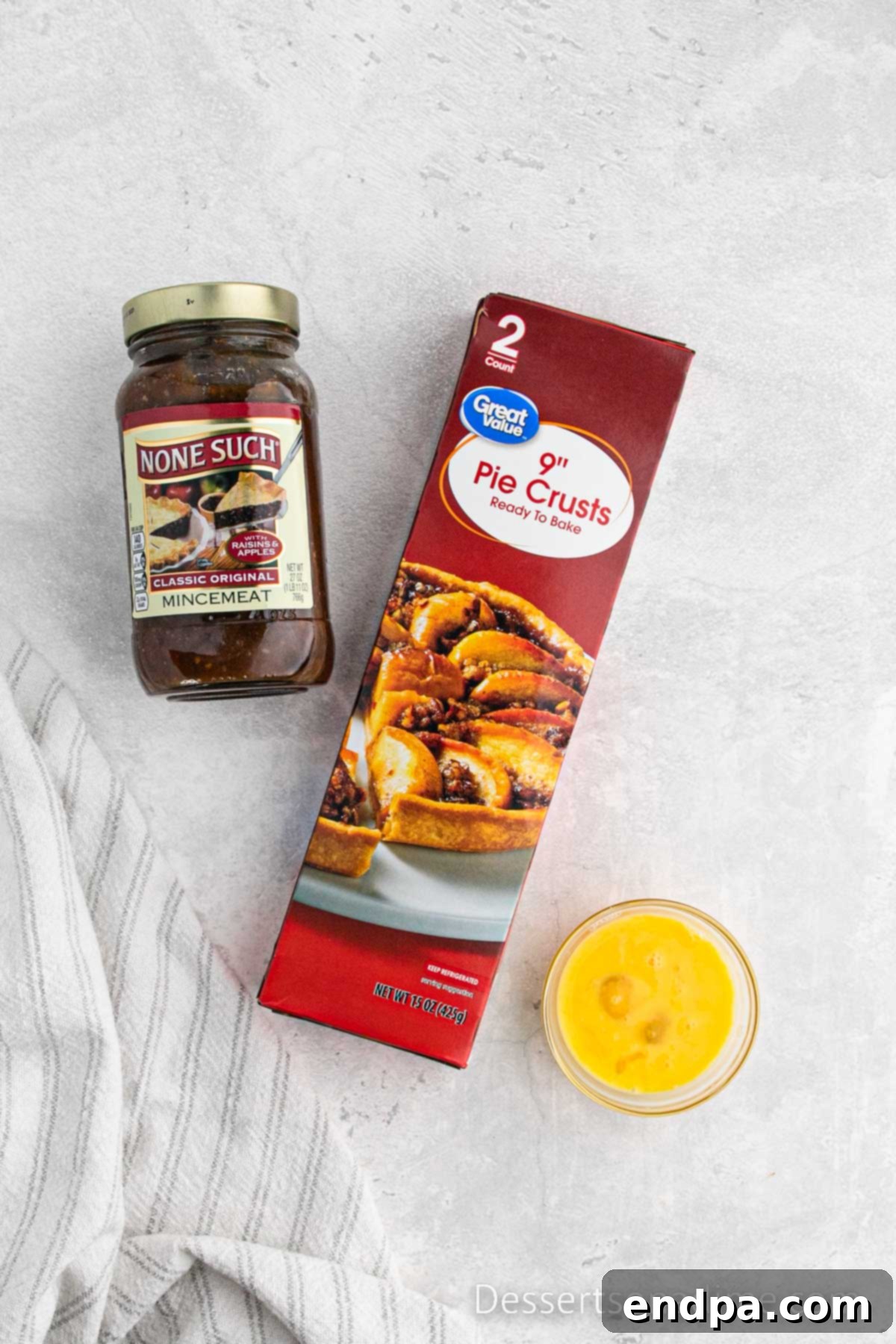 Traditional Christmas Mincemeat Pie 3 Key ingredients for mincemeat pie laid out on a table: pie crusts, jarred mincemeat, and an egg.