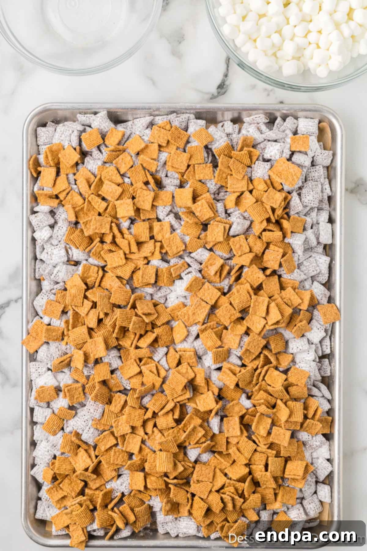 Smores Indulgence Mix 10 S'mores Puppy Chow on a baking sheet, with Golden Grahams sprinkled on top before mixing.