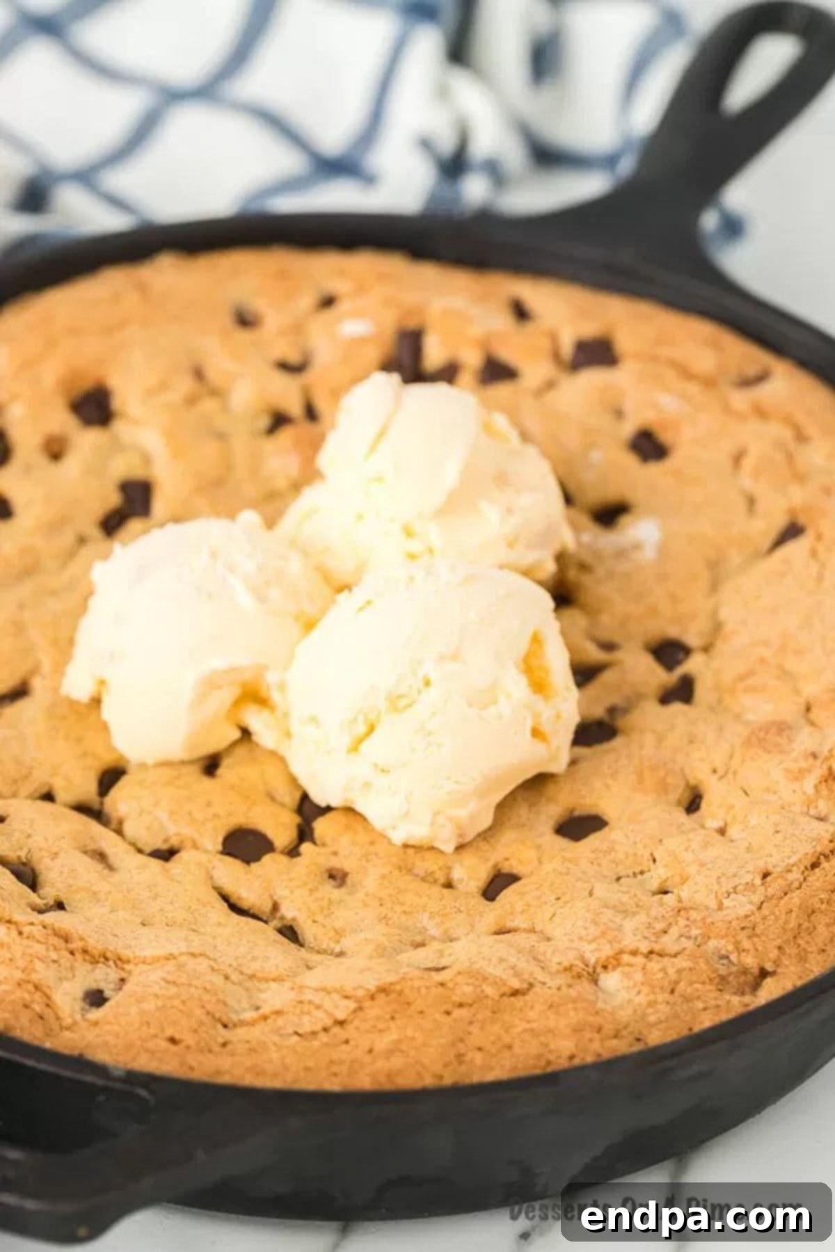 Warm chocolate chip pizookie baked in a cast iron skillet, topped with two scoops of melting vanilla ice cream and a drizzle of chocolate syrup.