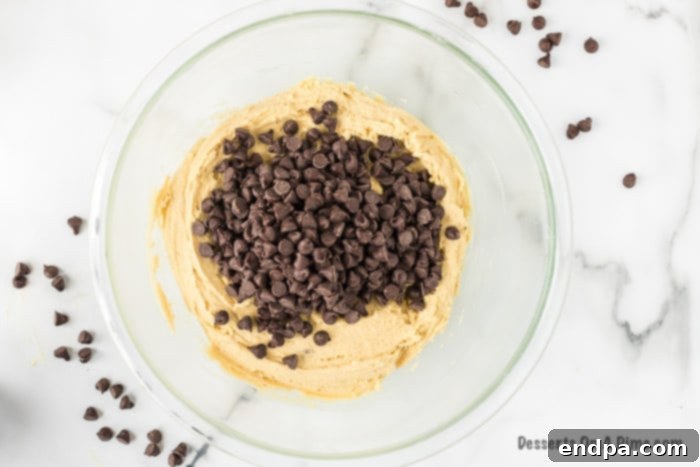 Chocolate chips being gently folded into the cookie dough by hand in a large mixing bowl.