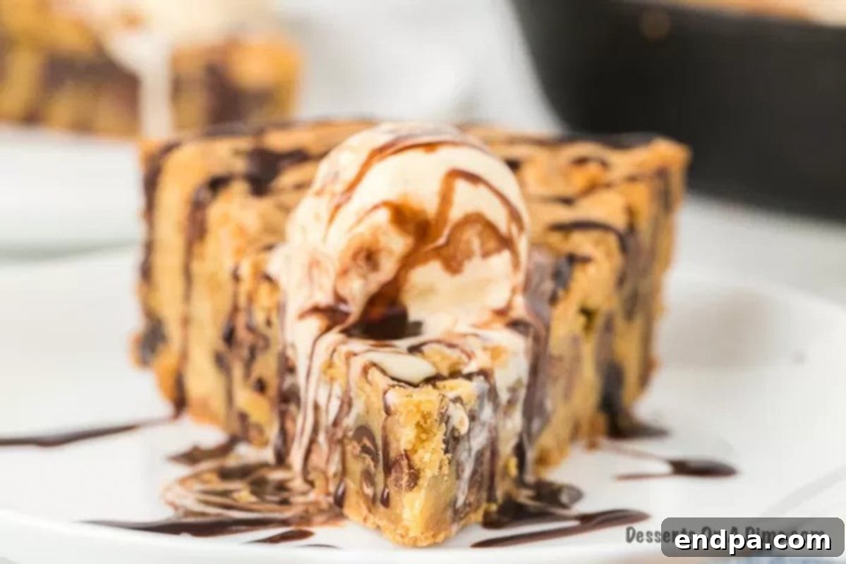 A serving of chocolate chip pizookie, freshly baked in a cast iron skillet, topped with melting vanilla ice cream and a rich chocolate syrup drizzle.