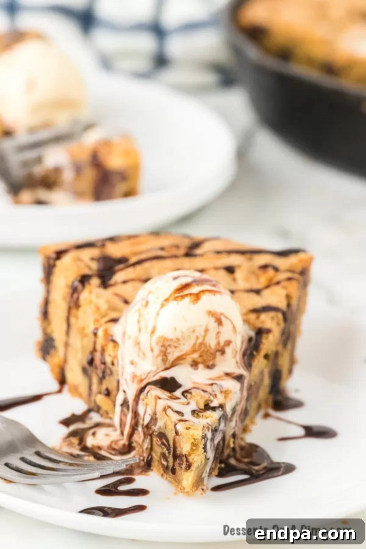 A beautifully presented slice of chocolate chip pizookie, rich with melted chocolate, topped with two scoops of vanilla ice cream and generously drizzled with chocolate syrup, ready to be enjoyed.