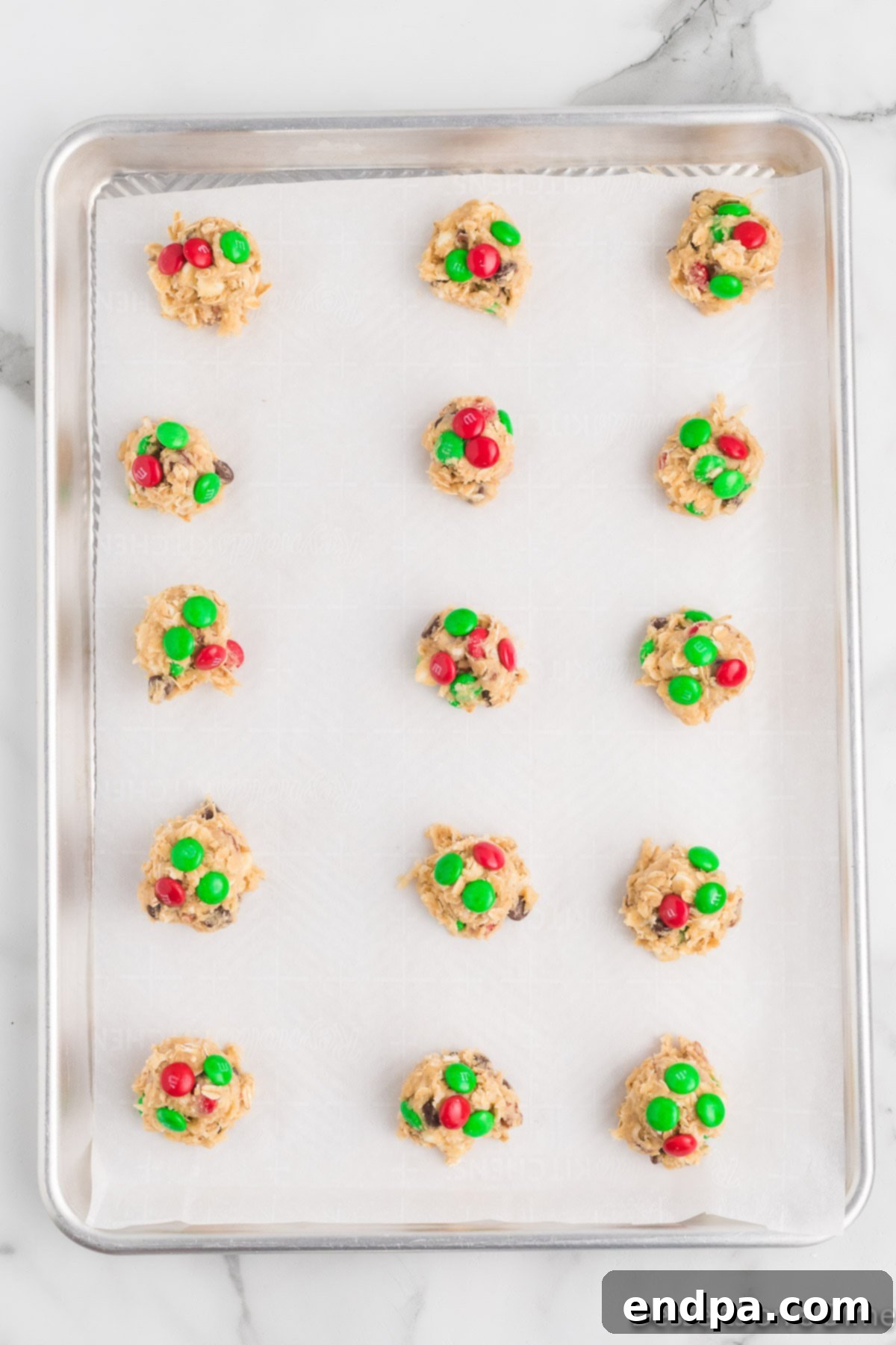 Festive Frontier Cookies 9 Pressing additional red and green M&M's into the tops of the scooped cookie dough balls on a baking sheet before baking.