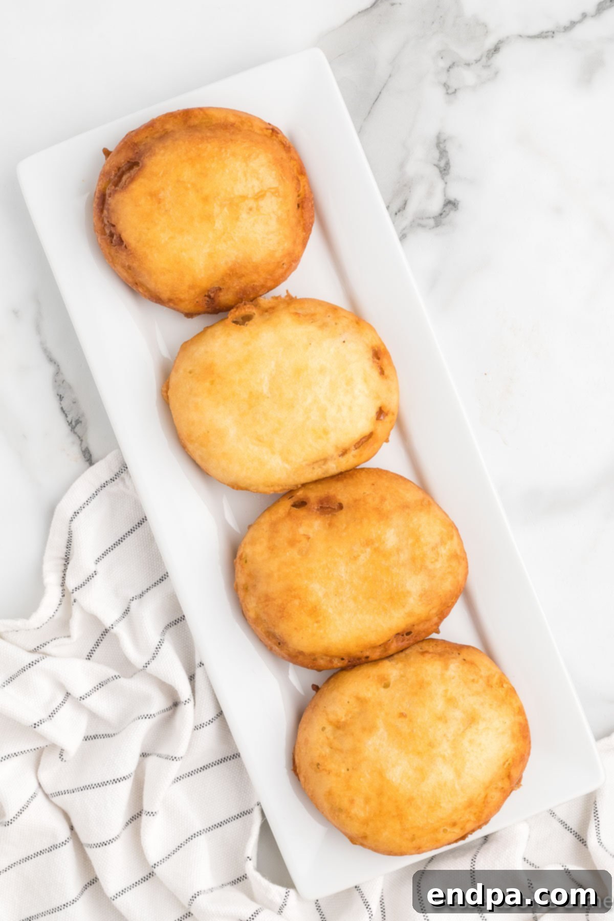 Freshly fried honey buns resting on a platter lined with paper towels to absorb excess oil.