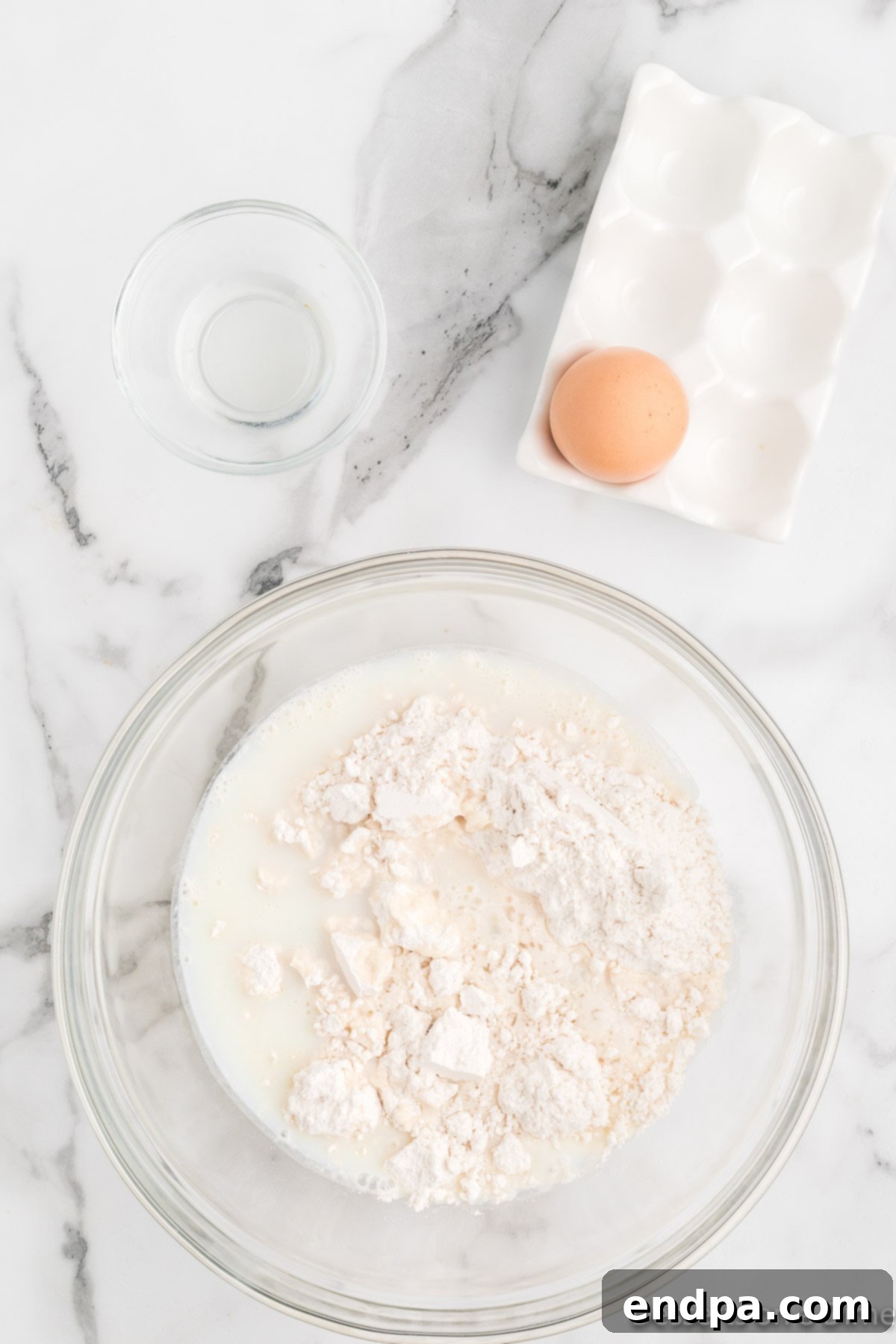 Milk and vegetable oil being added to the pancake mix and egg in the mixing bowl.