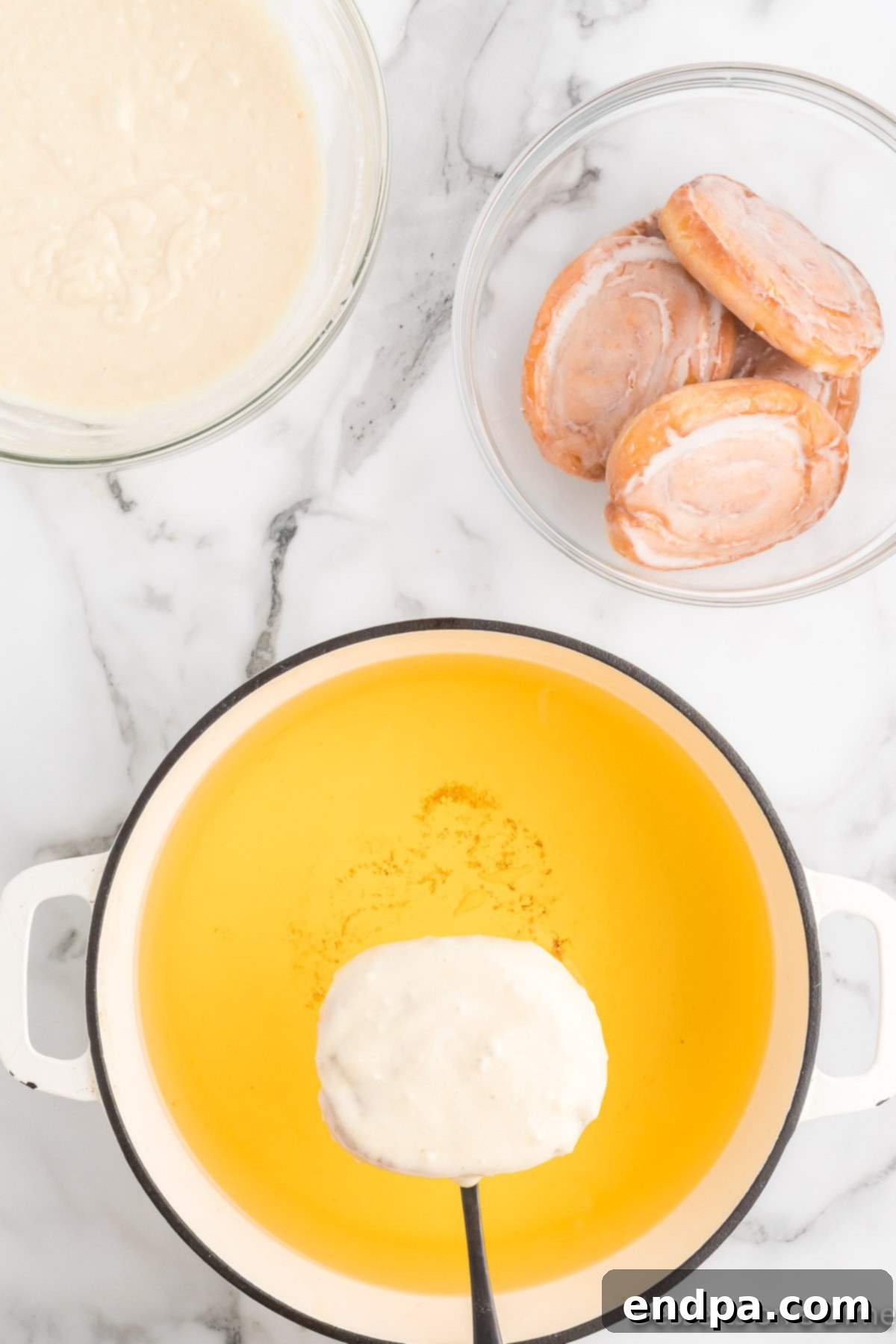 A batter-coated honey bun being gently lowered into a pot of hot oil for frying.