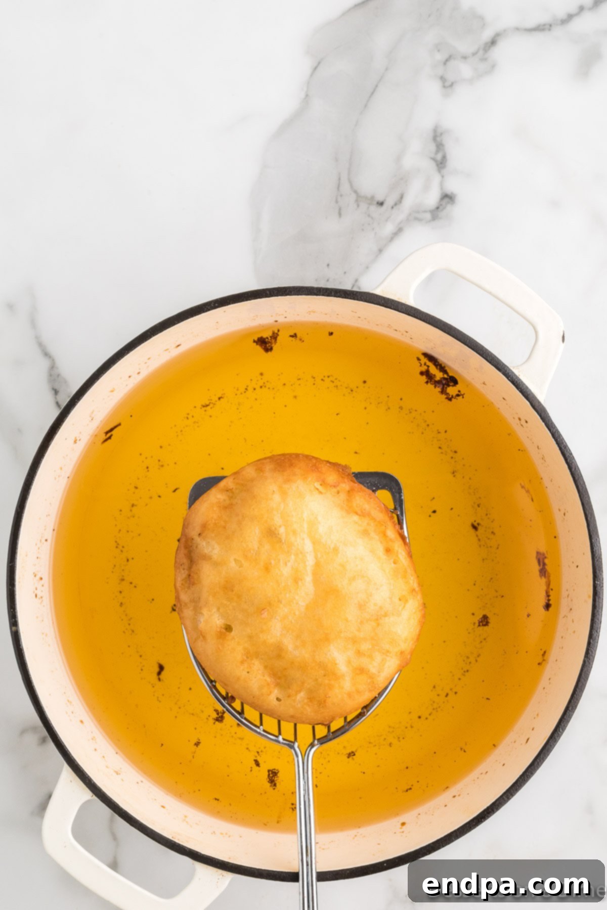 A fried honey bun being removed from the hot oil with tongs, golden brown and crispy.
