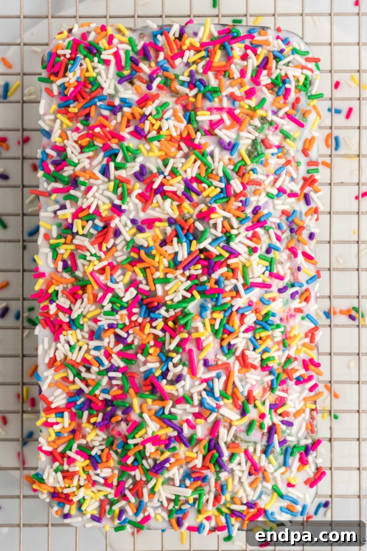 Rainbow sprinkles covering the icing on the unicorn bread, sitting on a wire rack.