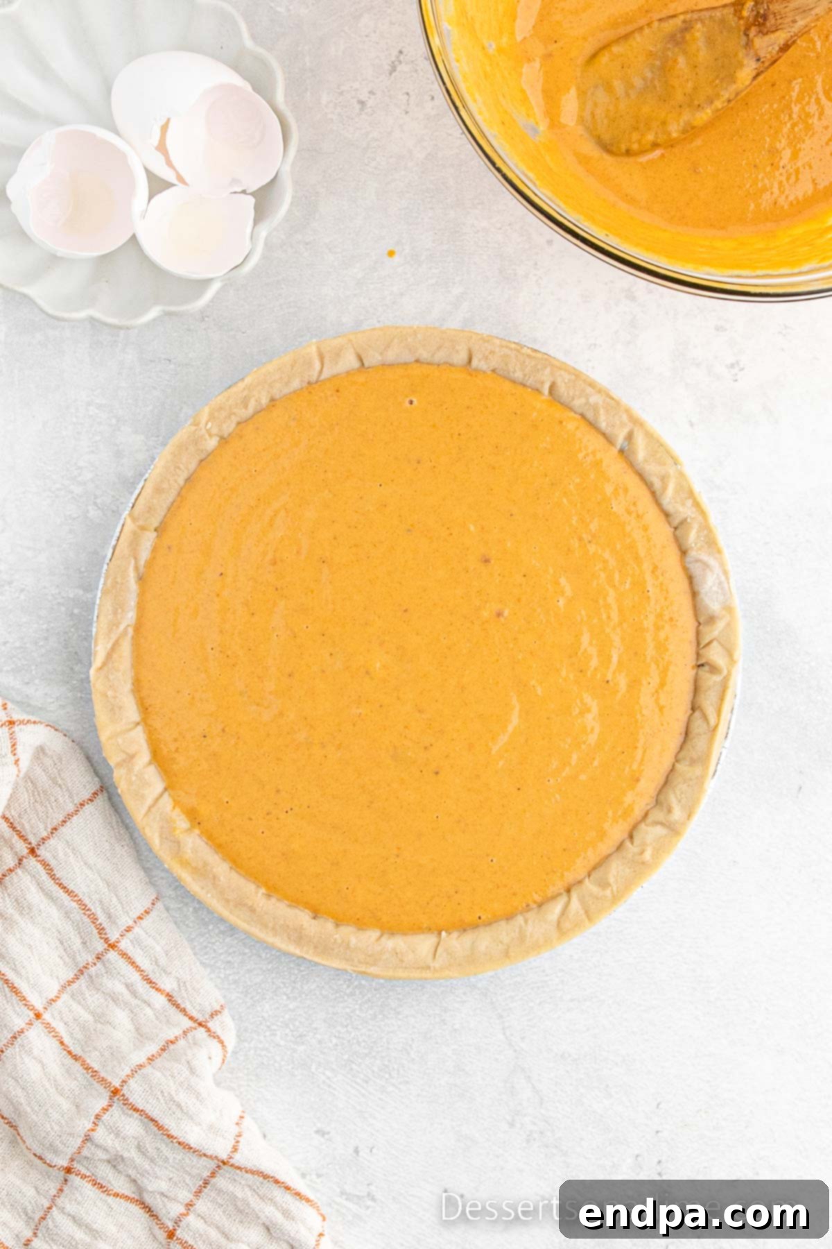 The smooth pumpkin pie mixture being poured into an unbaked pie crust in a pie pan.