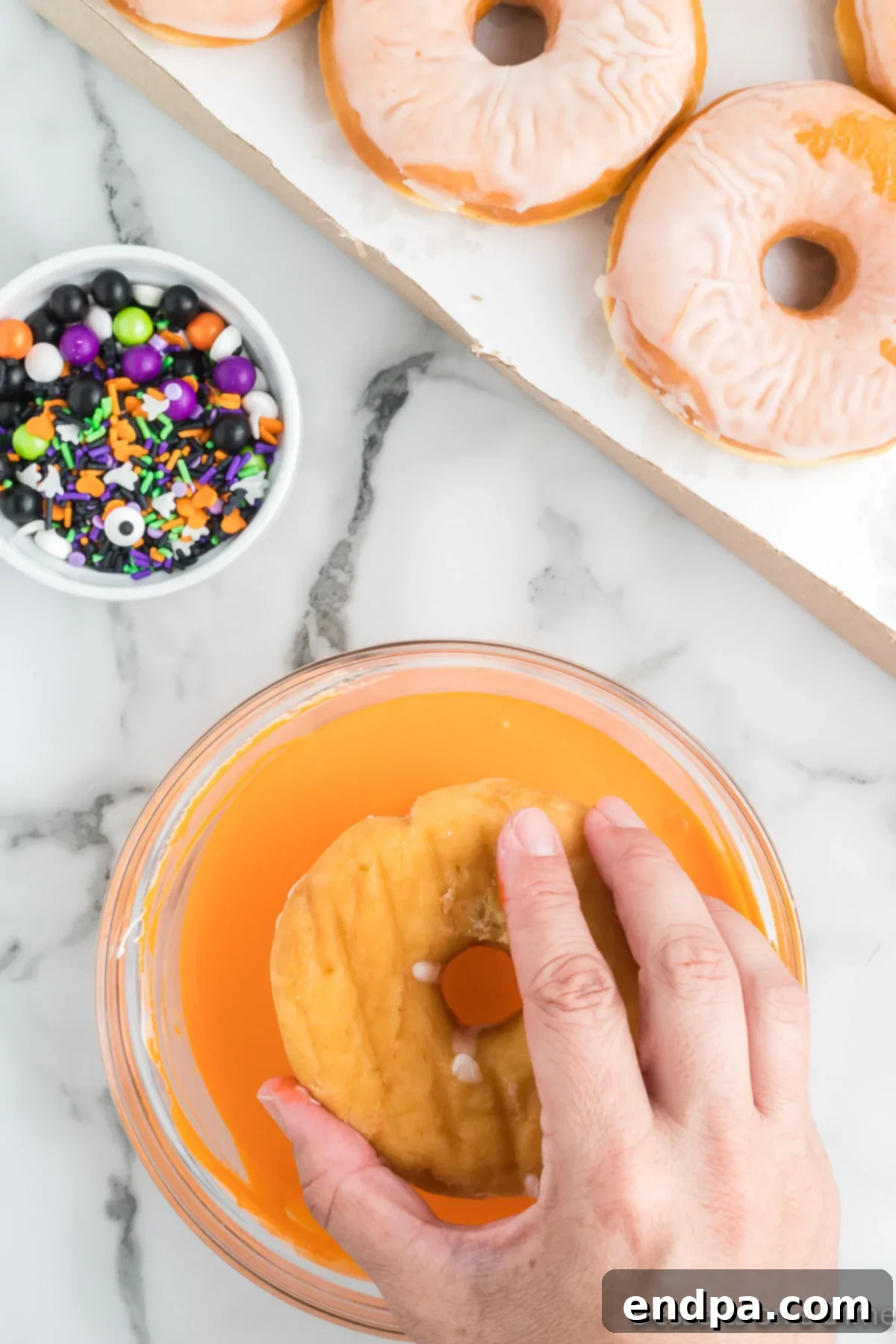 Spooky Delicious Halloween Donuts 6 Donut being dipped into orange frosting.