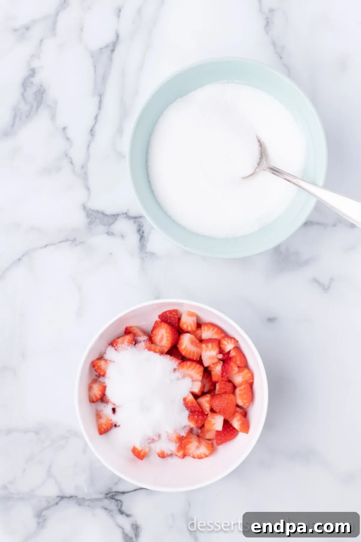 Diced strawberries and granulated sugar combined in a small bowl, beginning to release juices.