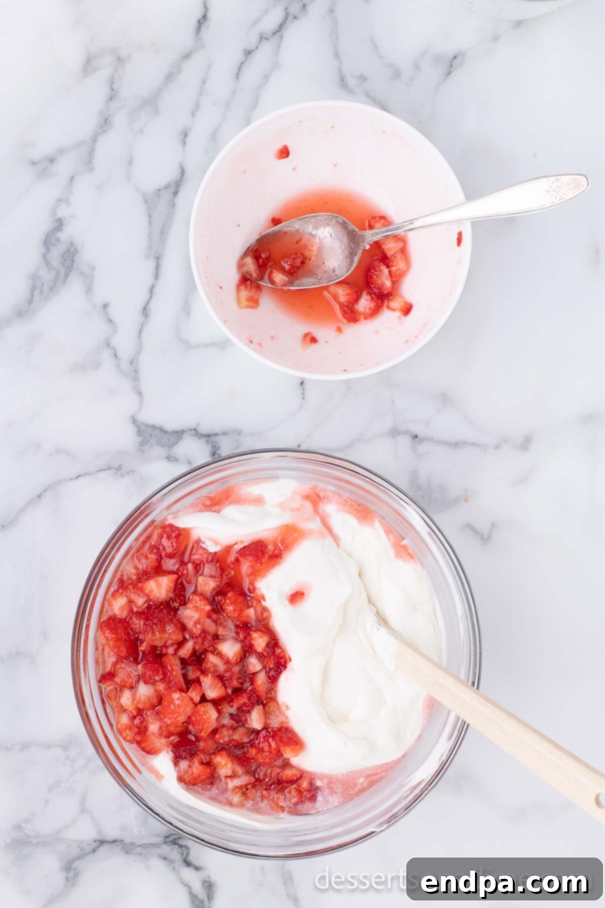 The macerated strawberry mixture being added to the combined whipped cream and condensed milk.