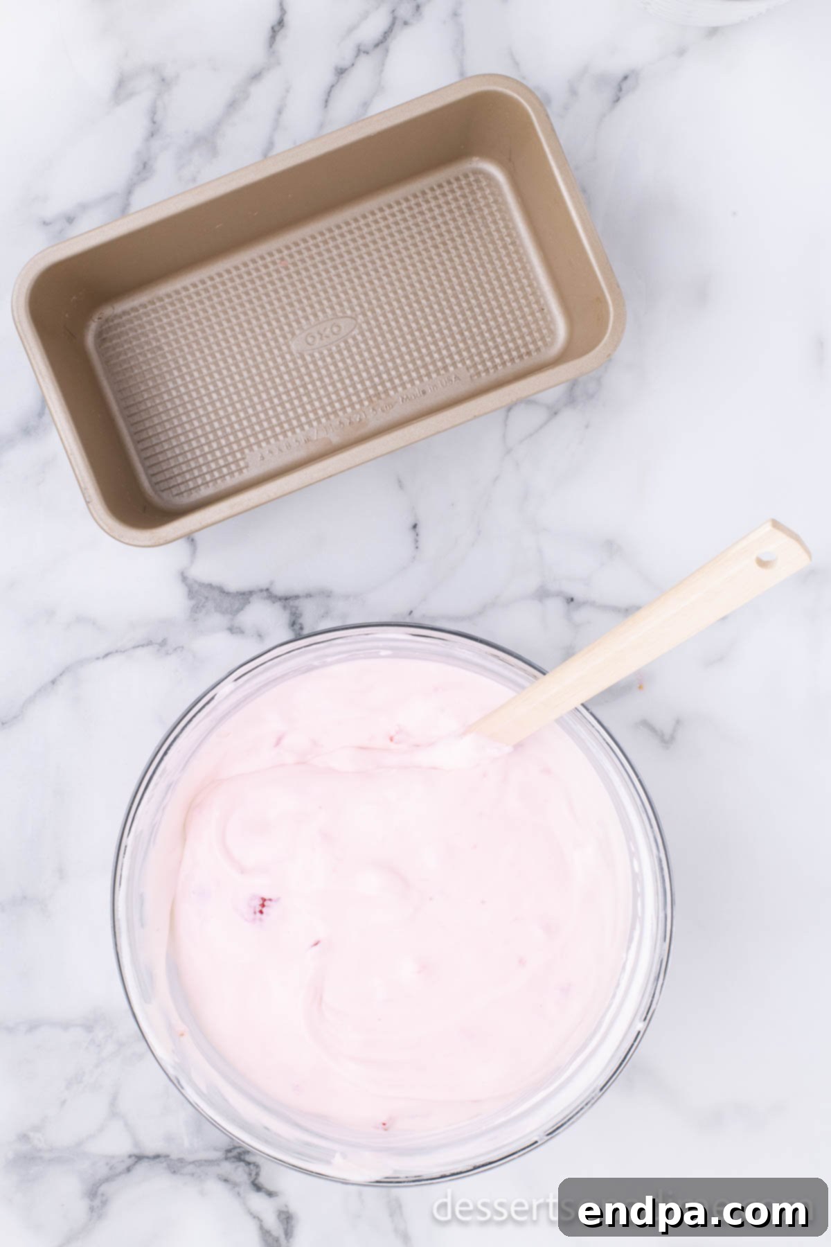 The ice cream mixture being gently folded with a rubber spatula in a bowl to fully combine ingredients.