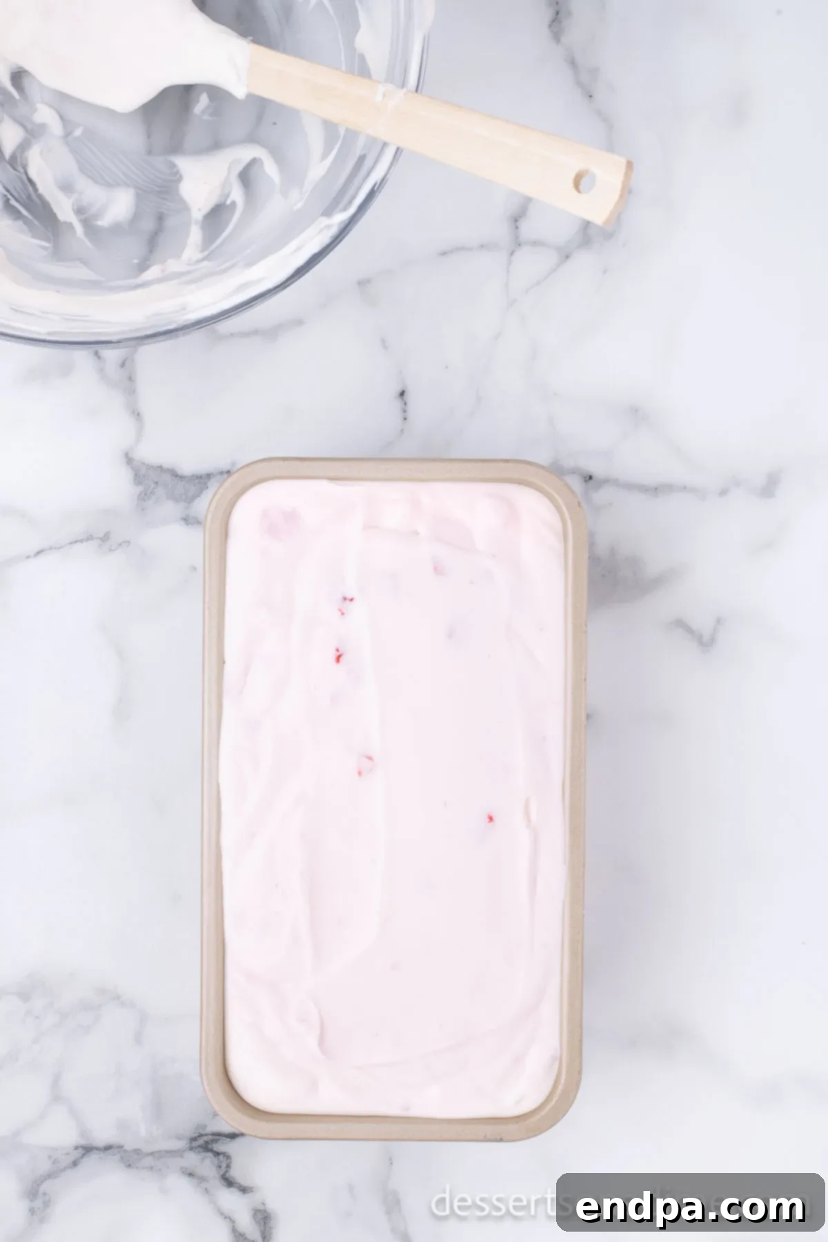 The smooth strawberry ice cream mixture being spread evenly into a loaf pan for freezing.
