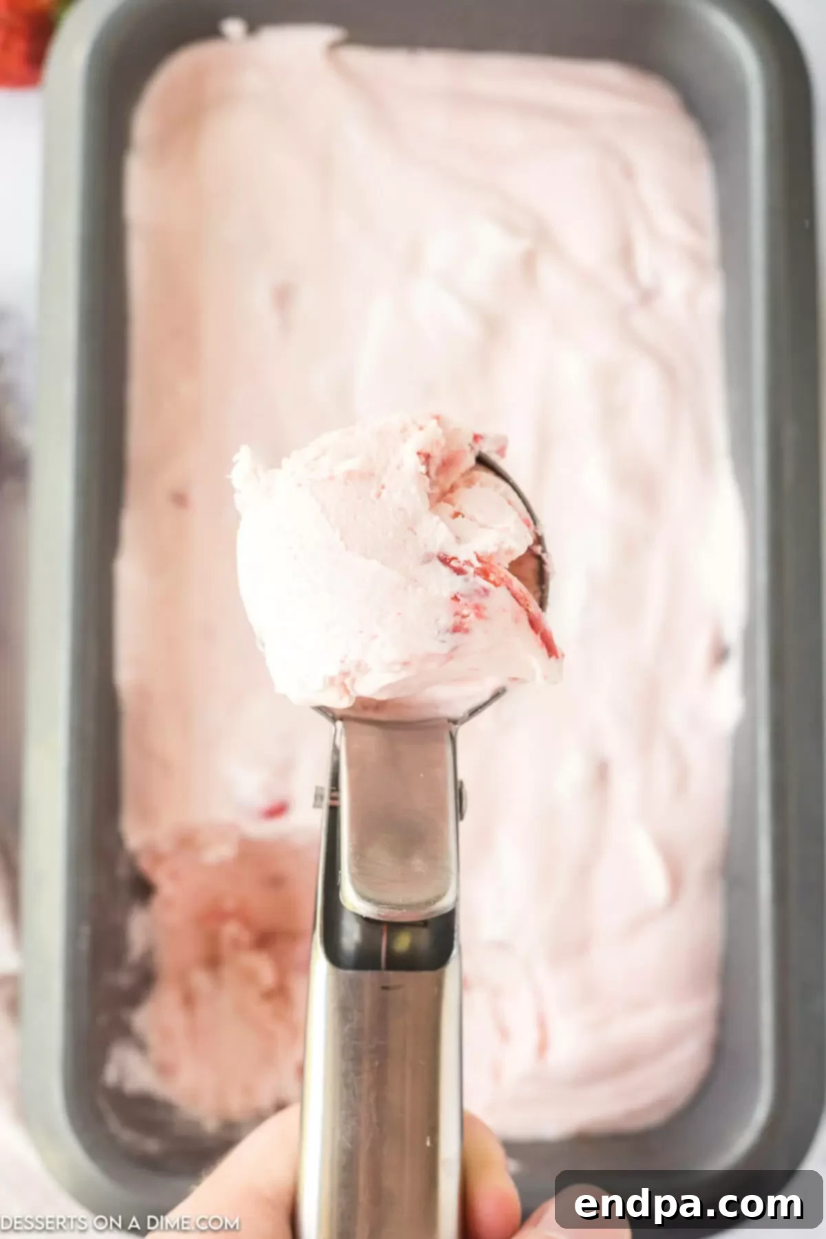 A scoop of No-Churn Strawberry Ice Cream being taken from the loaf pan after freezing.