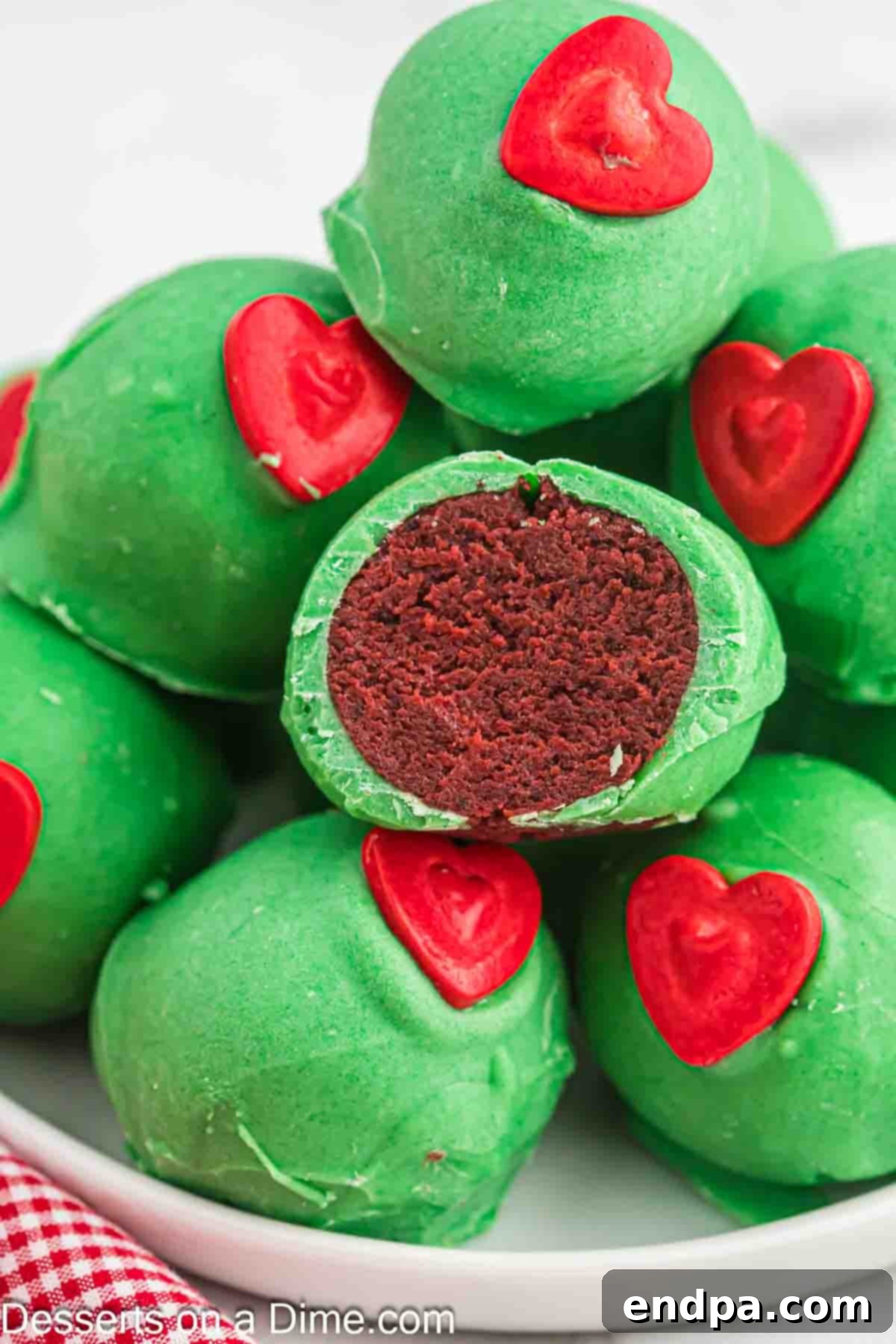 Grinchmas Cake Bites 2 Vibrant green Grinch Cake Balls with red candy hearts on a festive white plate, ready for holiday serving.